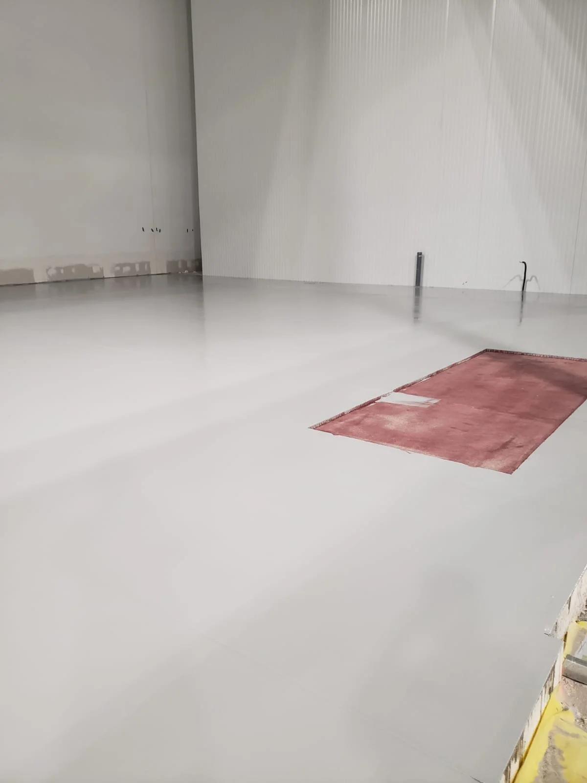 Empty room with freshly painted white floor and walls, a red rectangular section on the floor, and construction materials nearby.