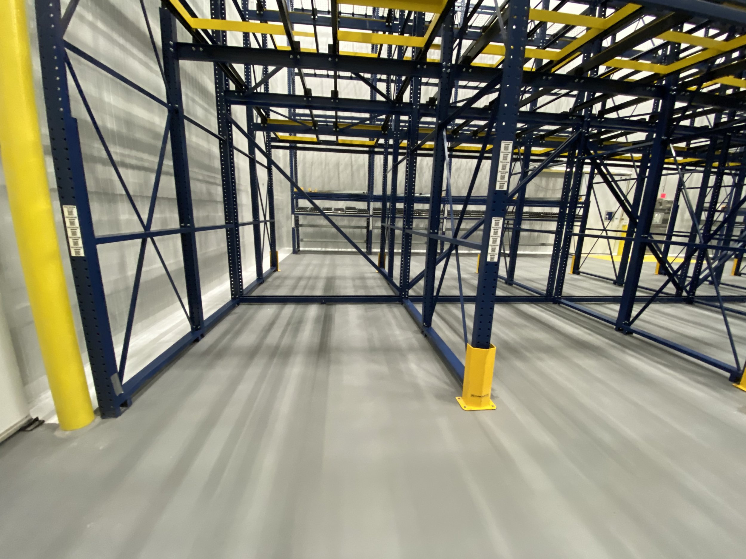 Empty warehouse shelving units with blue and yellow frames and gray floors.