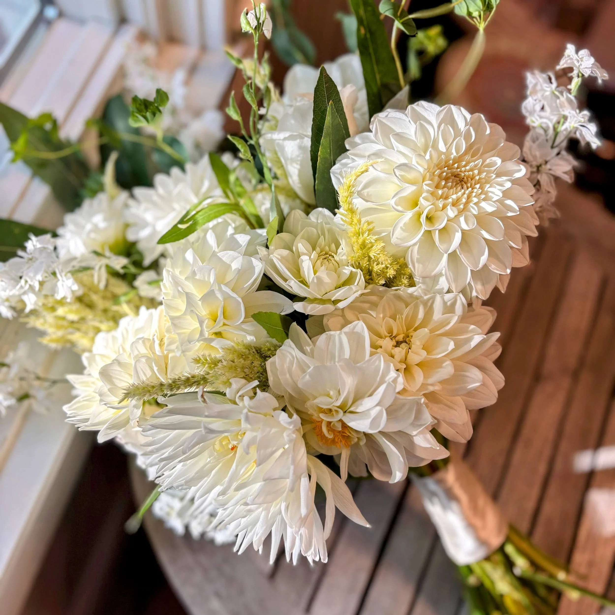 Close-up of a bouquet of white dahlias, roses, and greenery on a wooden table.