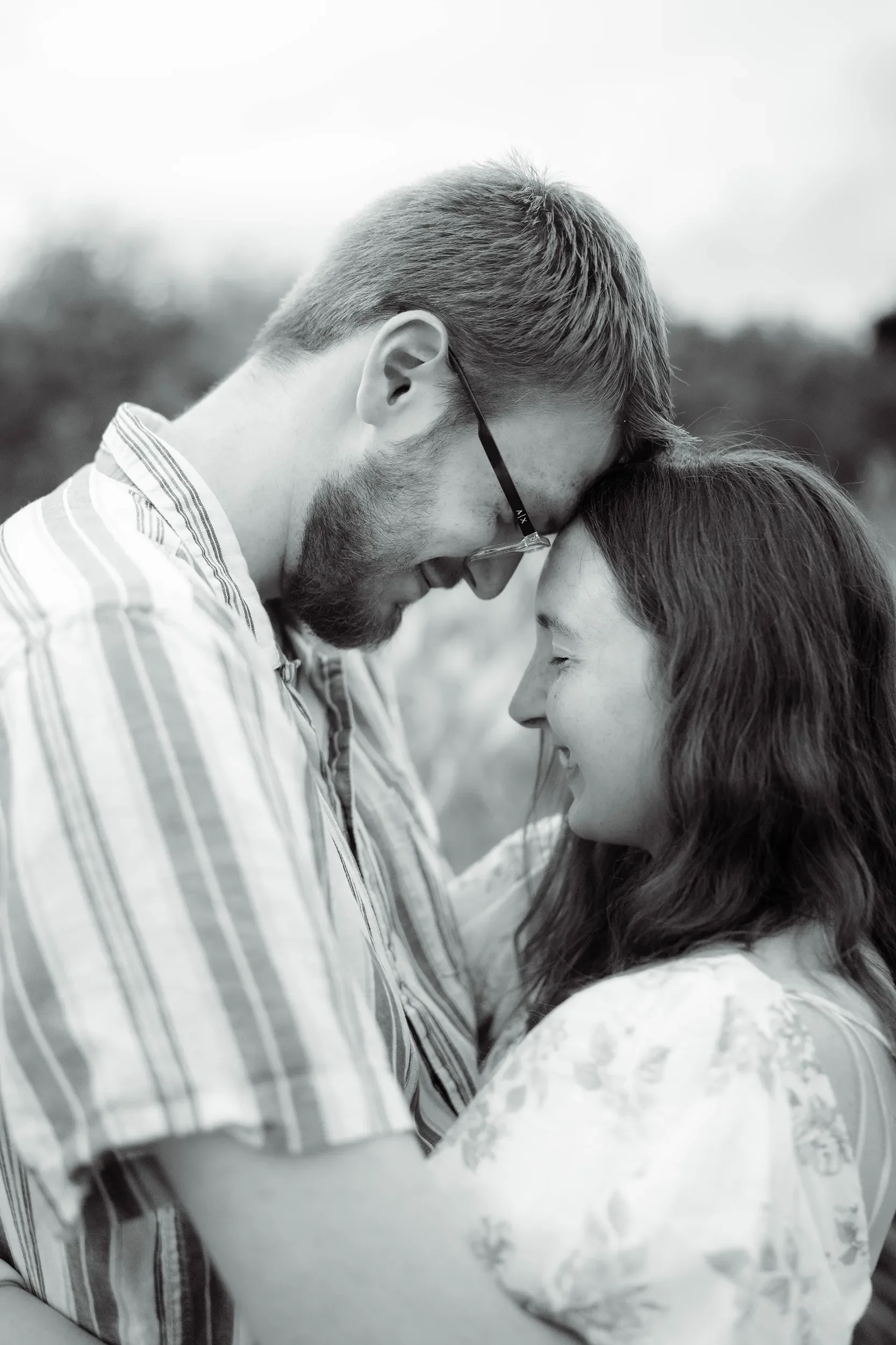 A black and white photo of a man and woman holding each other with foreheads touching, smiling softly and with eyes closed.