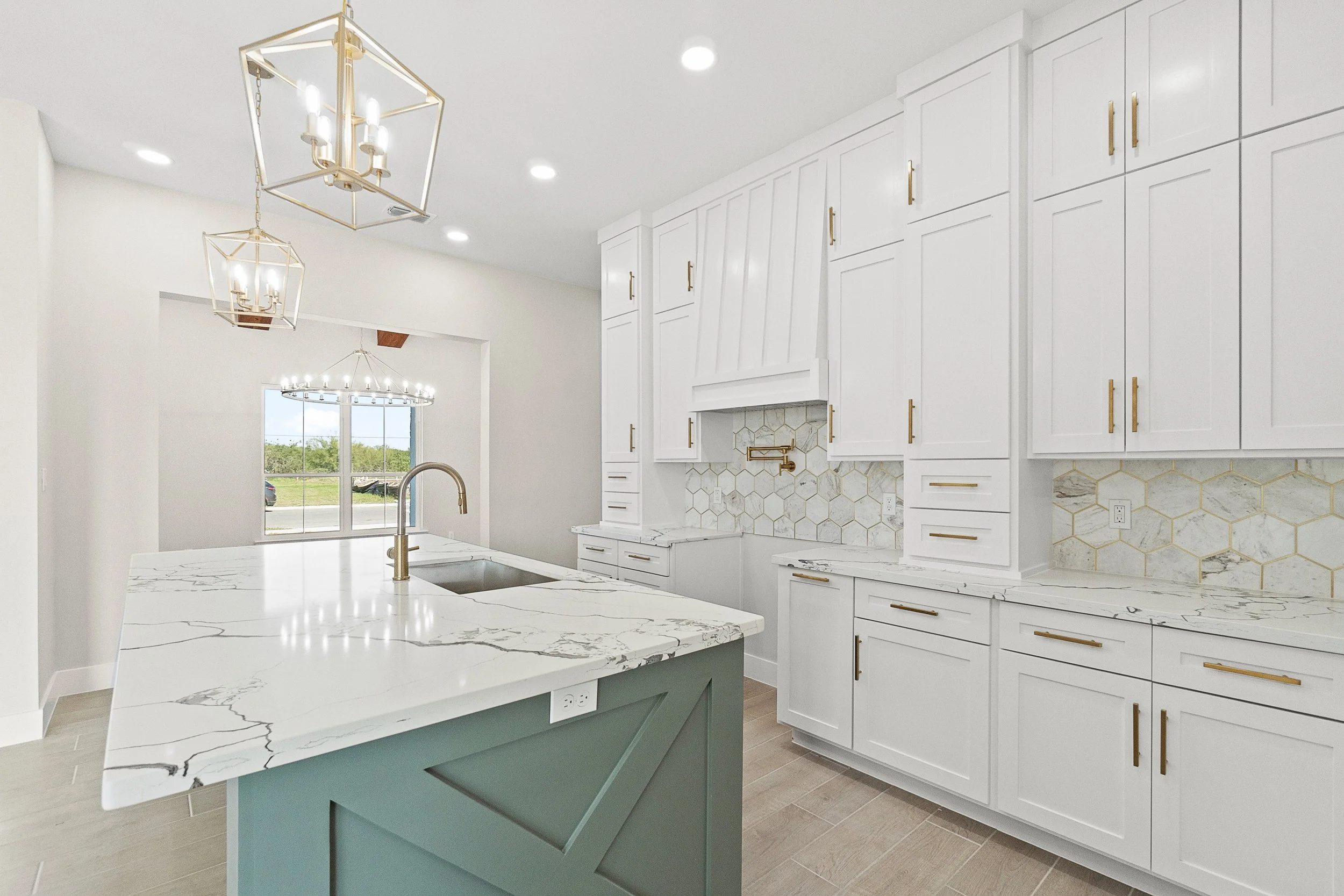 Modern kitchen with white cabinets, marble countertops, hexagonal tile backsplash, gold hardware, and pendant lighting over a central island.