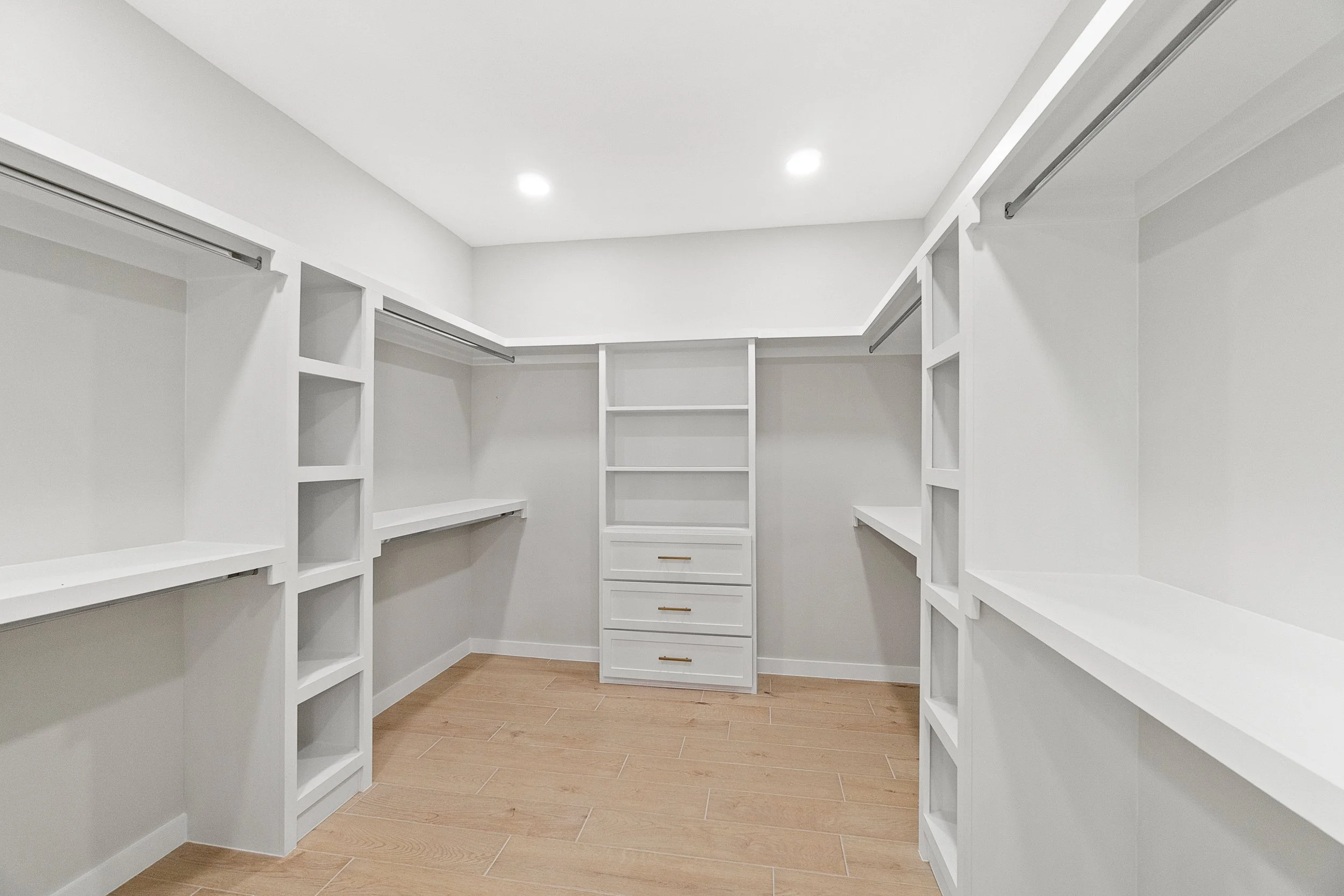 Empty white walk-in closet with wooden flooring, built-in shelves, and hanging rods.