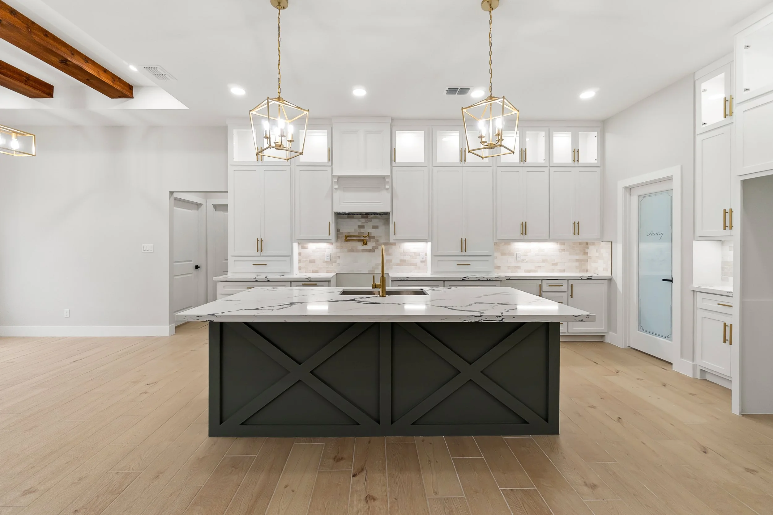 Modern white kitchen with a large island, light wood flooring, white cabinets, and gold accents.