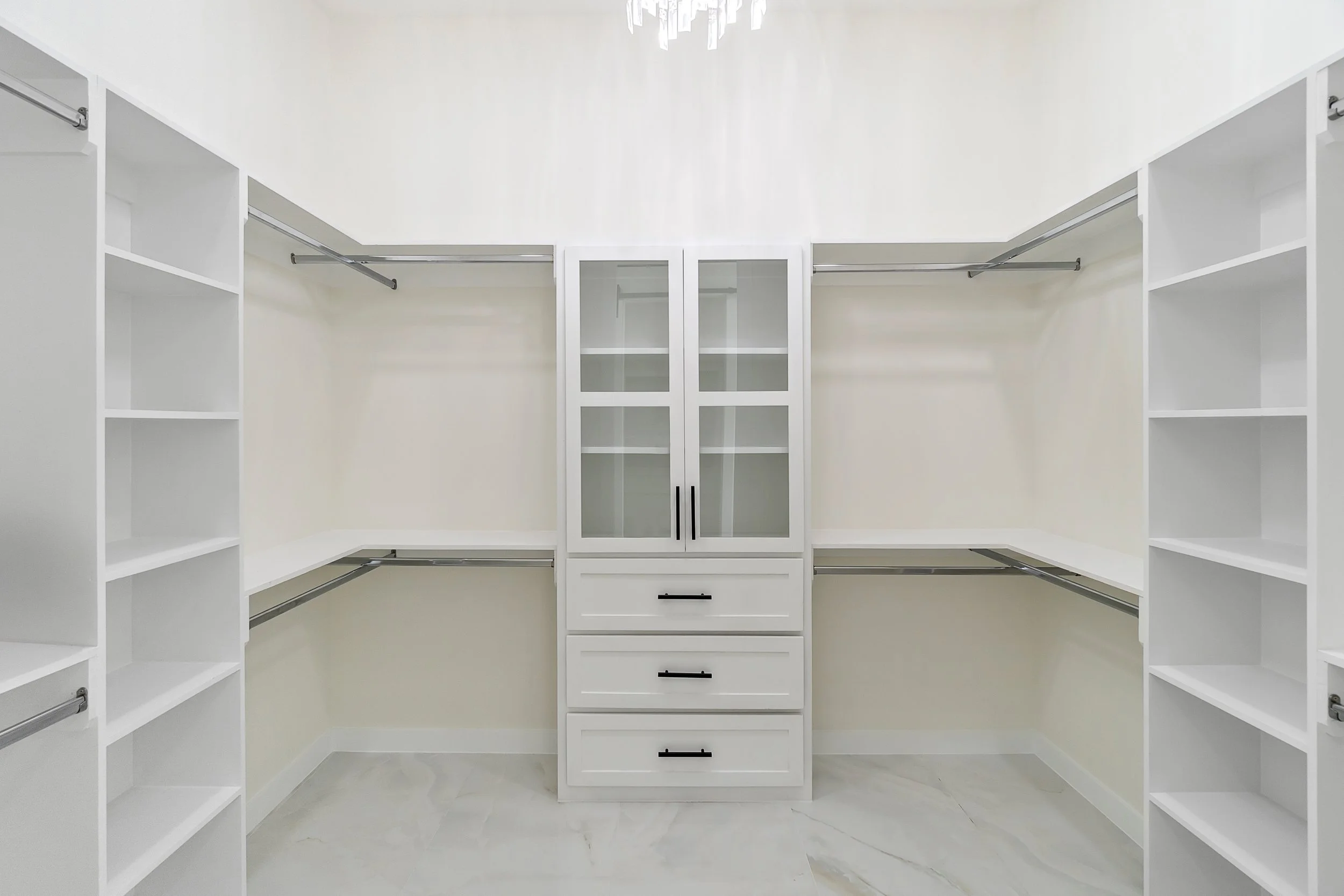 Empty white walk-in closet with built-in shelves, drawers, and hanging rods.