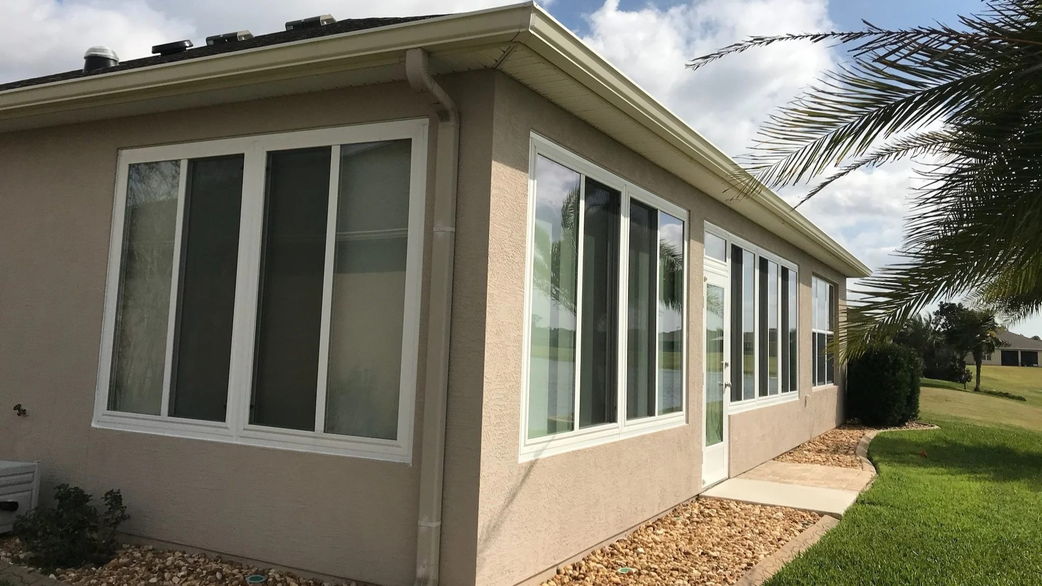 Backyard view of a house with a sunroom, surrounded by a well-maintained lawn, palm tree, and clear sky.