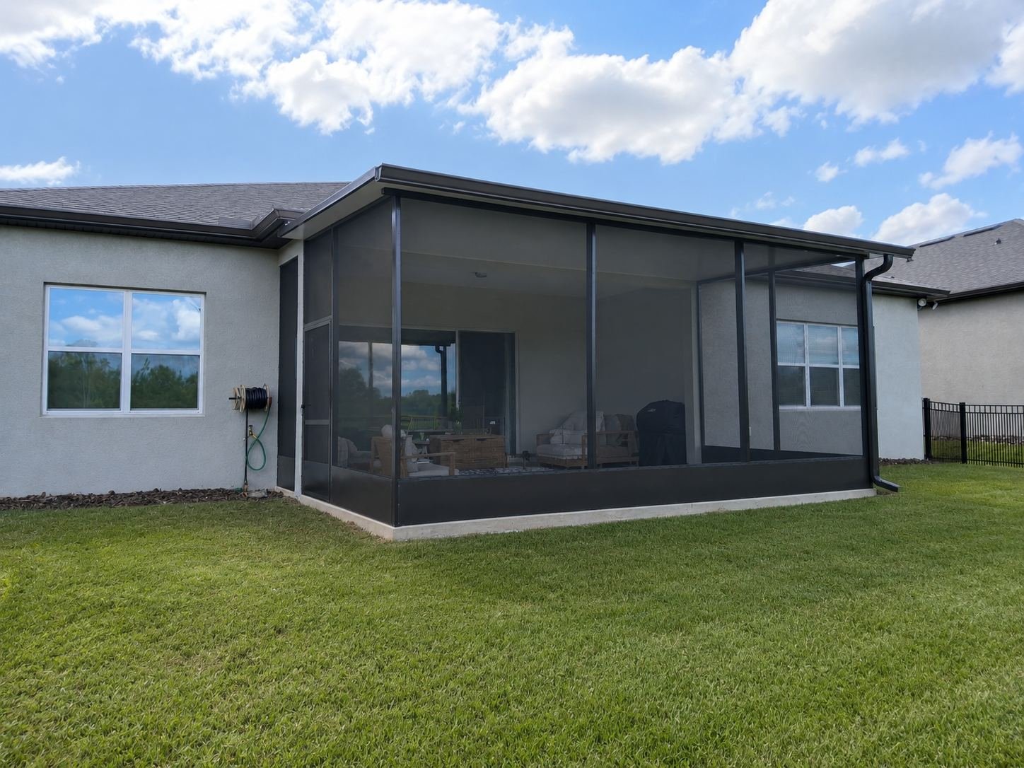A backyard with a house featuring a screened room, a lawn, a stone flower bed, and a blue sky with clouds.