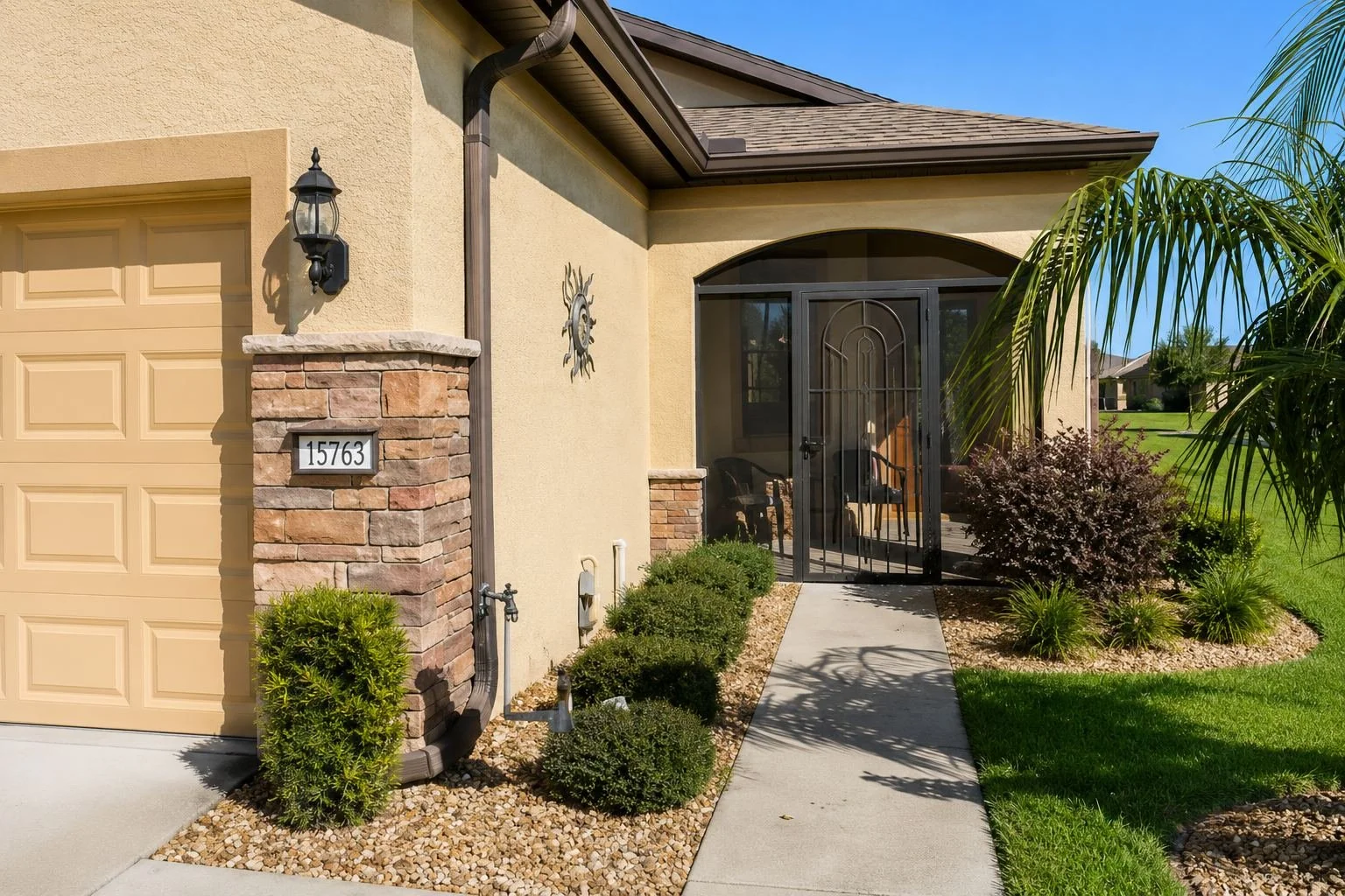 Front view of a house with a screened front porch, brick and stucco exterior, landscaped garden, and blue sky with clouds.