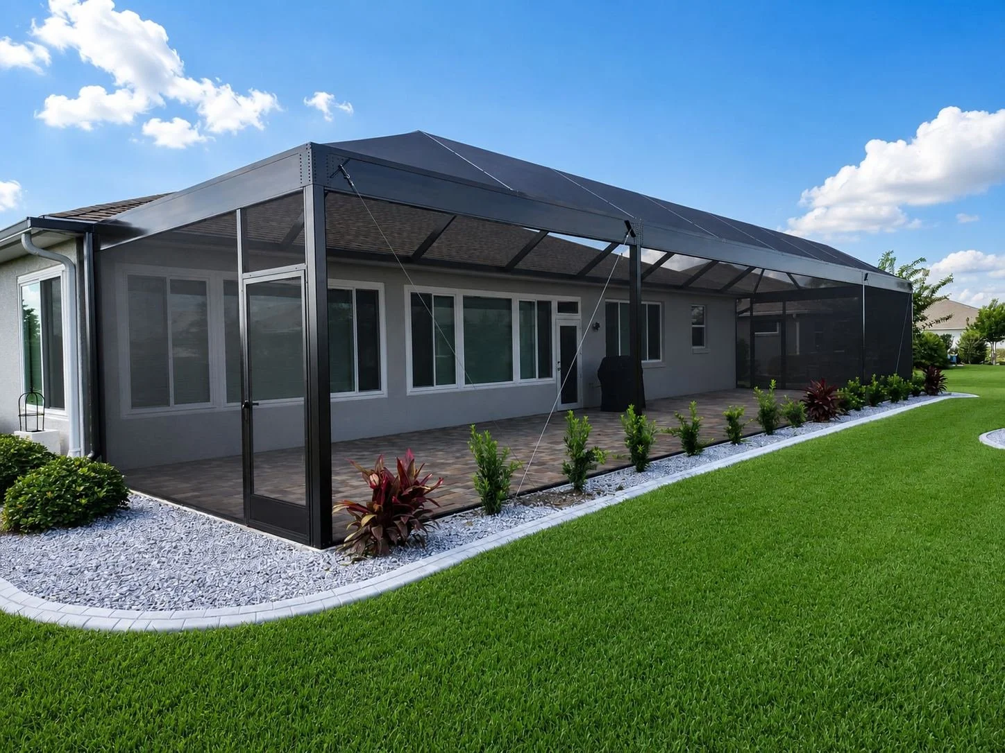 Backyard with screen cage, outdoor furniture, and a house in the background with a clear blue sky and some clouds.