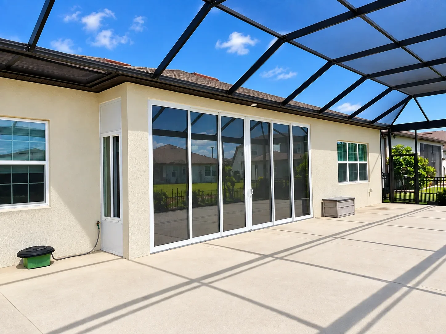 Backyard patio with large glass sliding doors, a screened enclosure roof, and neighboring houses visible.