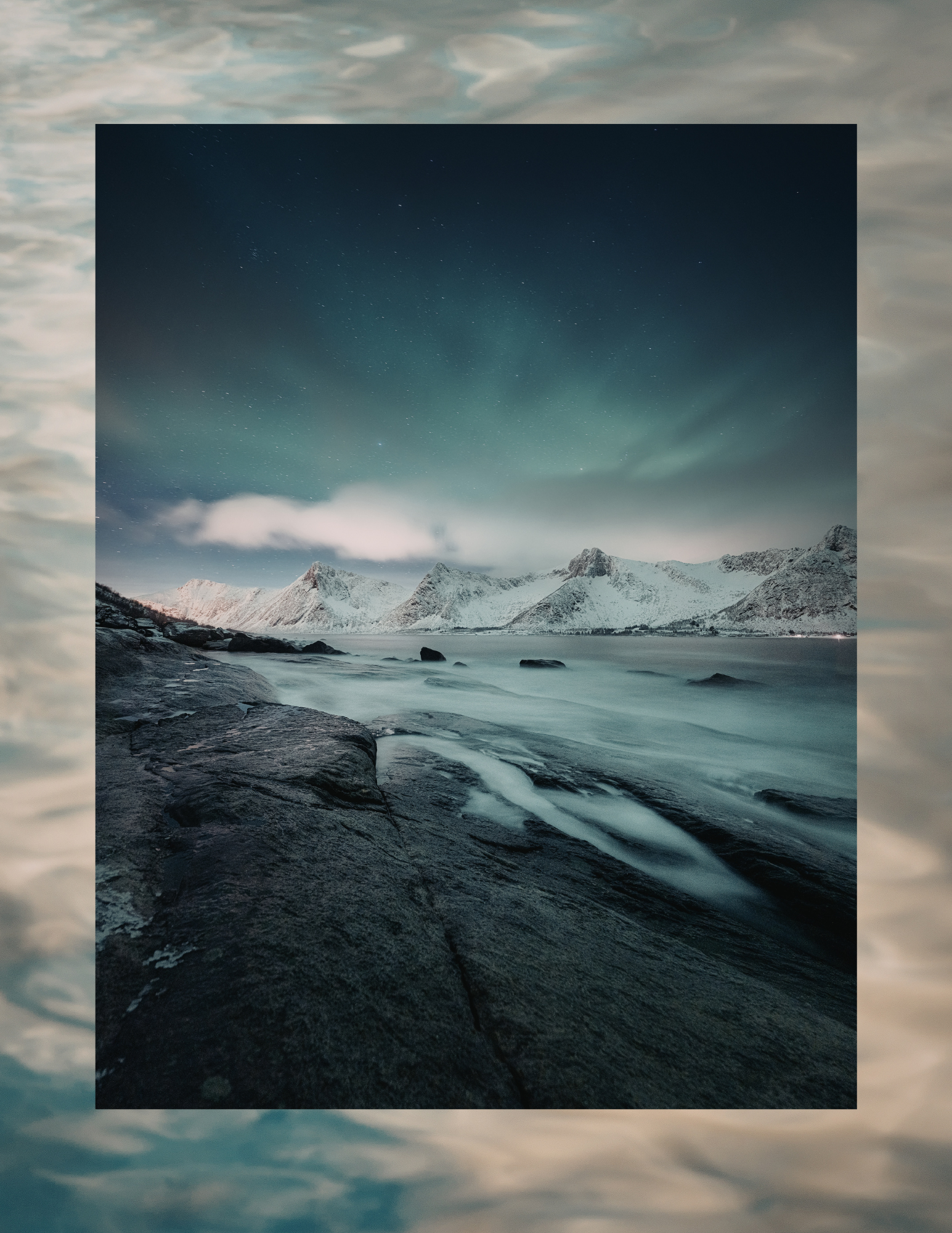 Nighttime landscape of a snow-covered mountain range, foggy water, and the Northern Lights in the sky.