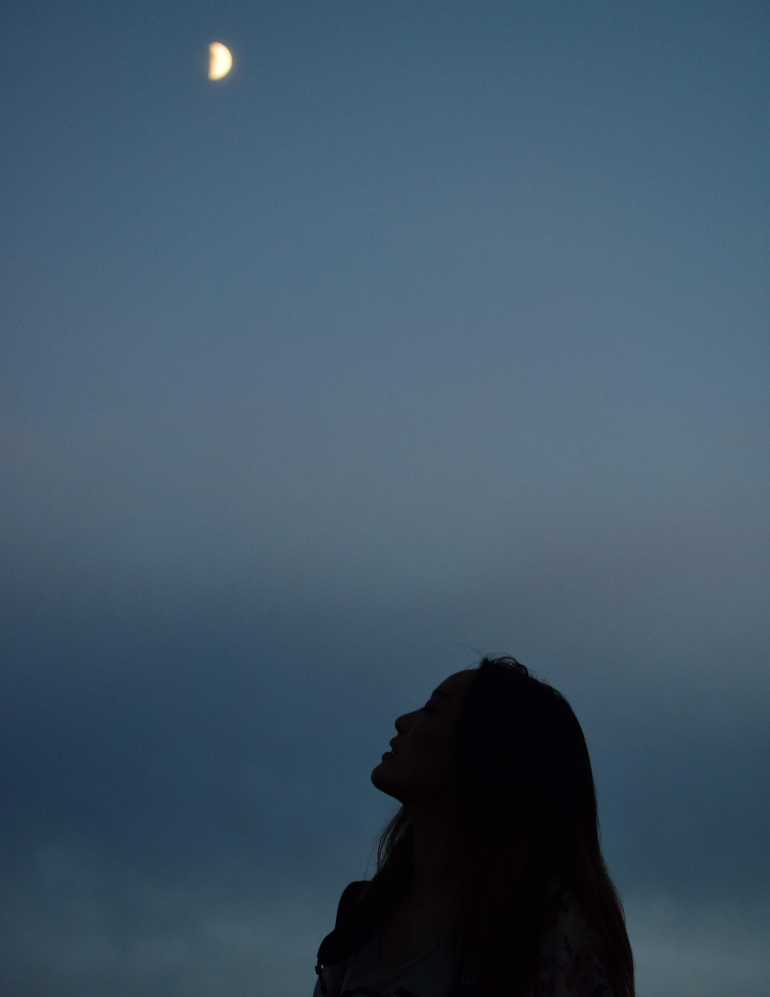 Silhouette of a woman looking at the moon at dusk.