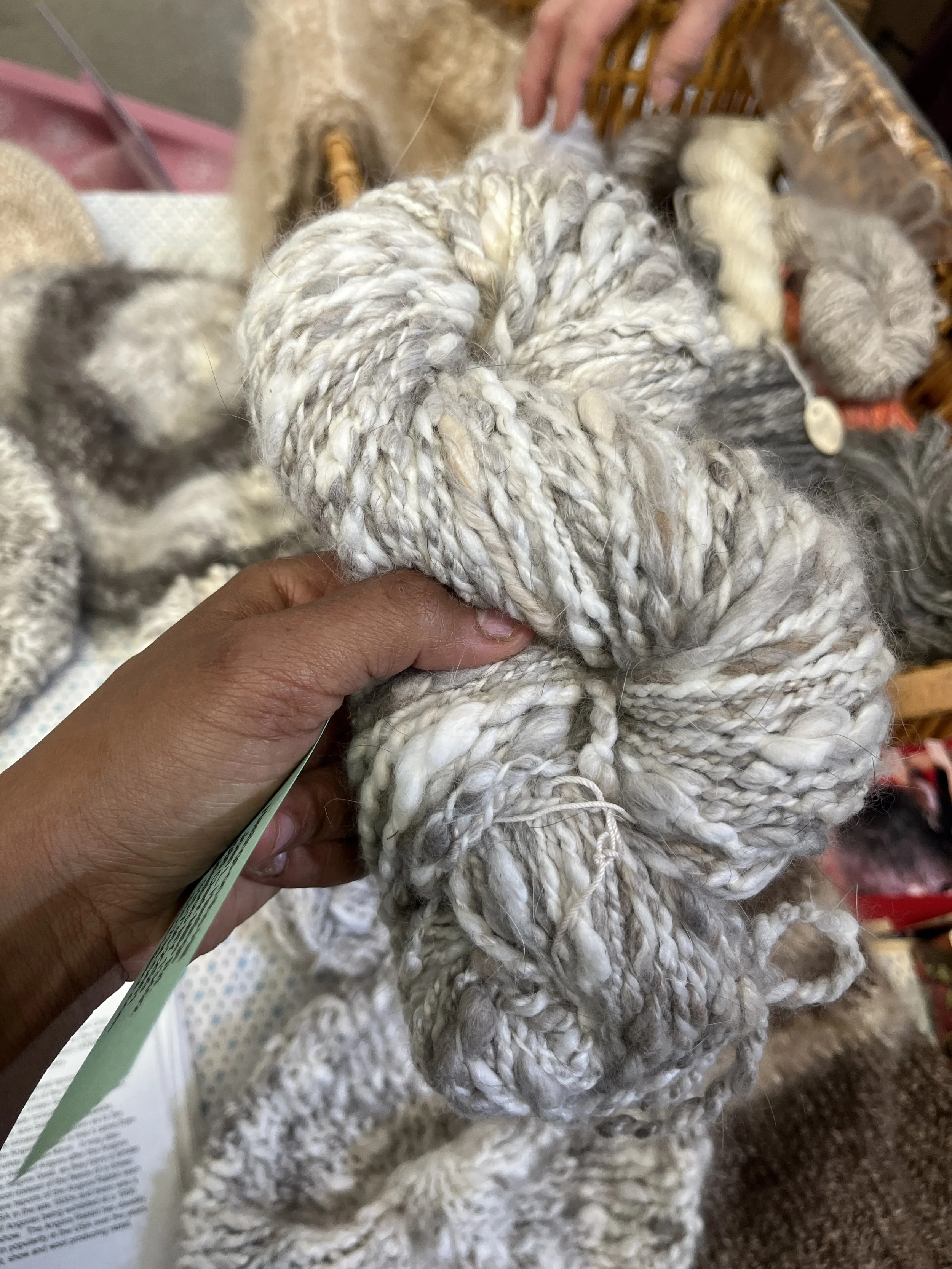 Close-up of a person holding raw, twisted wool yarn with more wool yarn on a table.