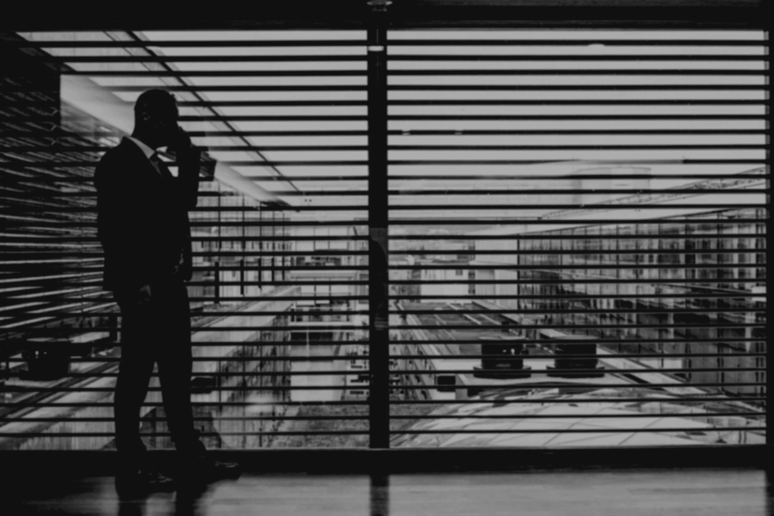 Silhouette of a man in a suit talking on the phone inside a building with horizontal bars in the foreground and cityscape in the background.