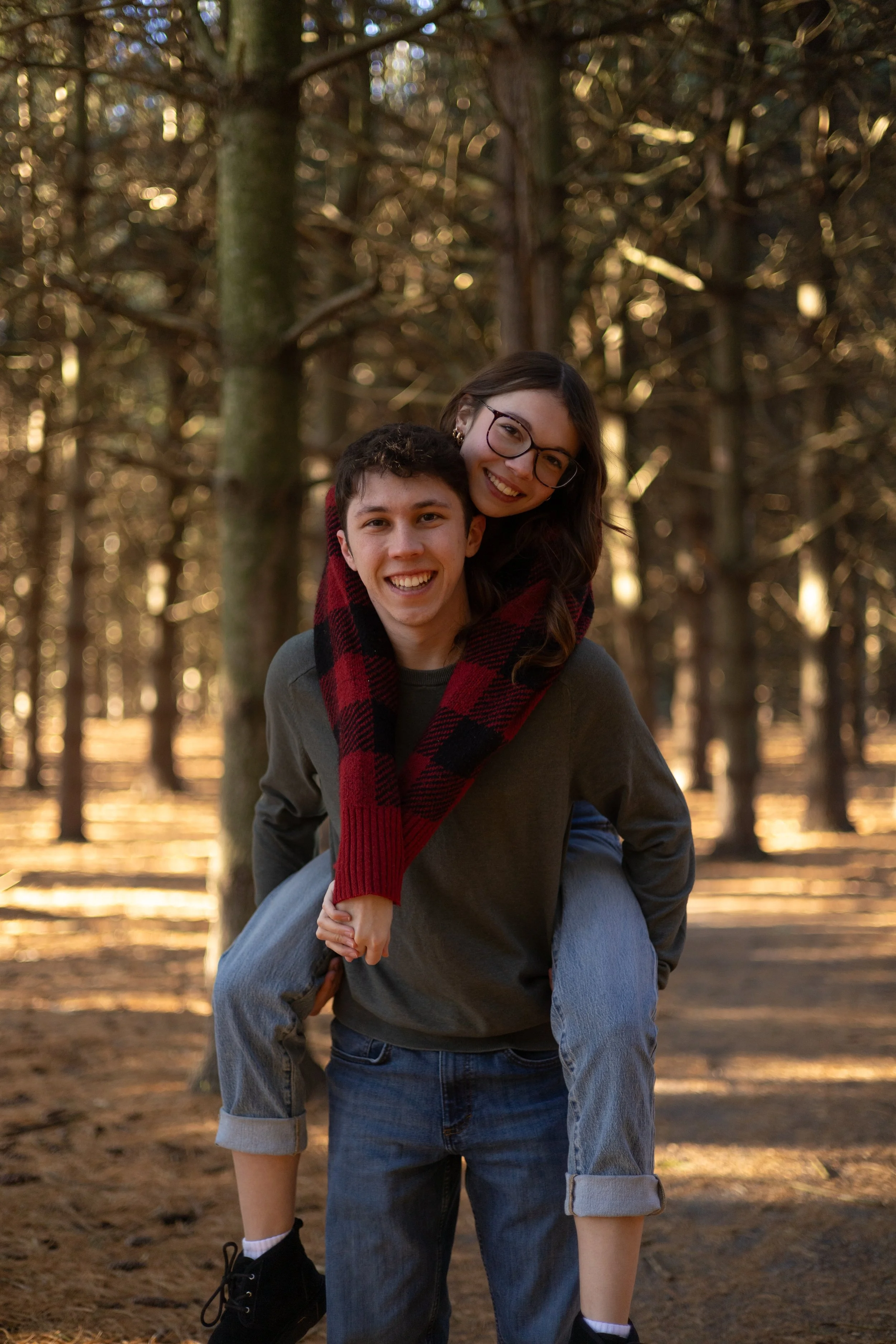 A young man giving a piggyback ride to a smiling young woman in a forest during autumn.