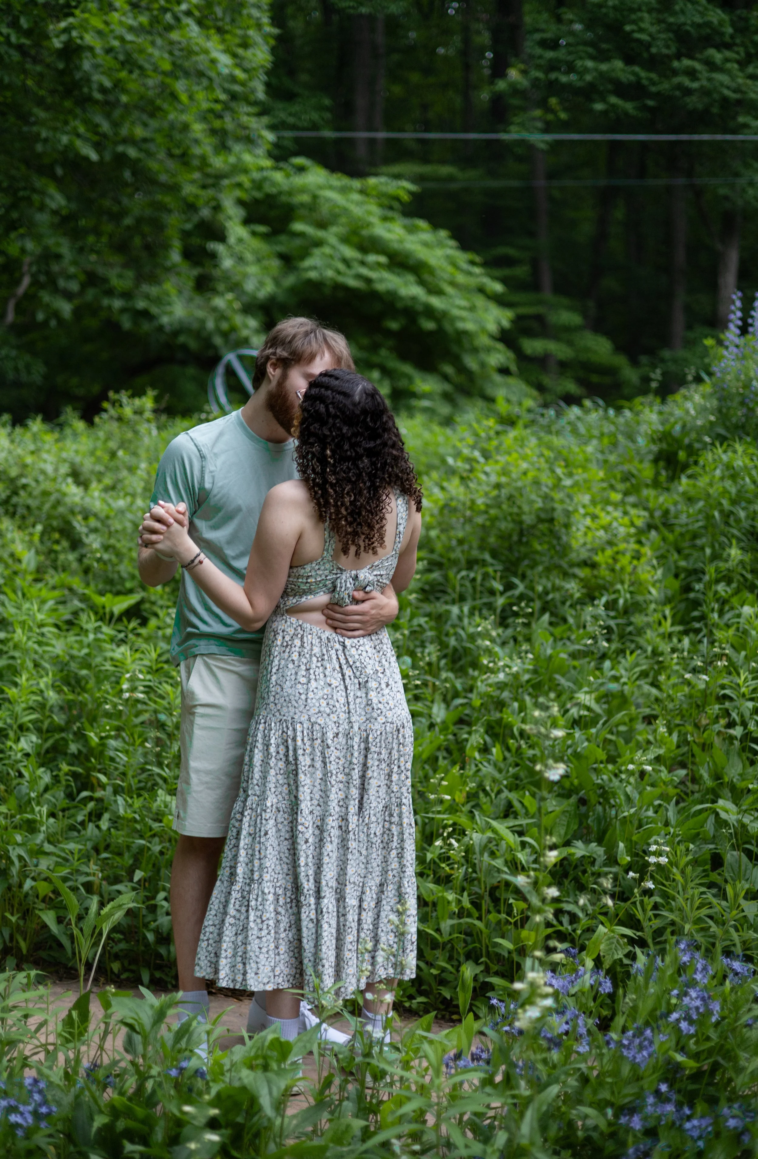 A couple dancing closely in a lush green garden surrounded by vibrant plants and flowers.
