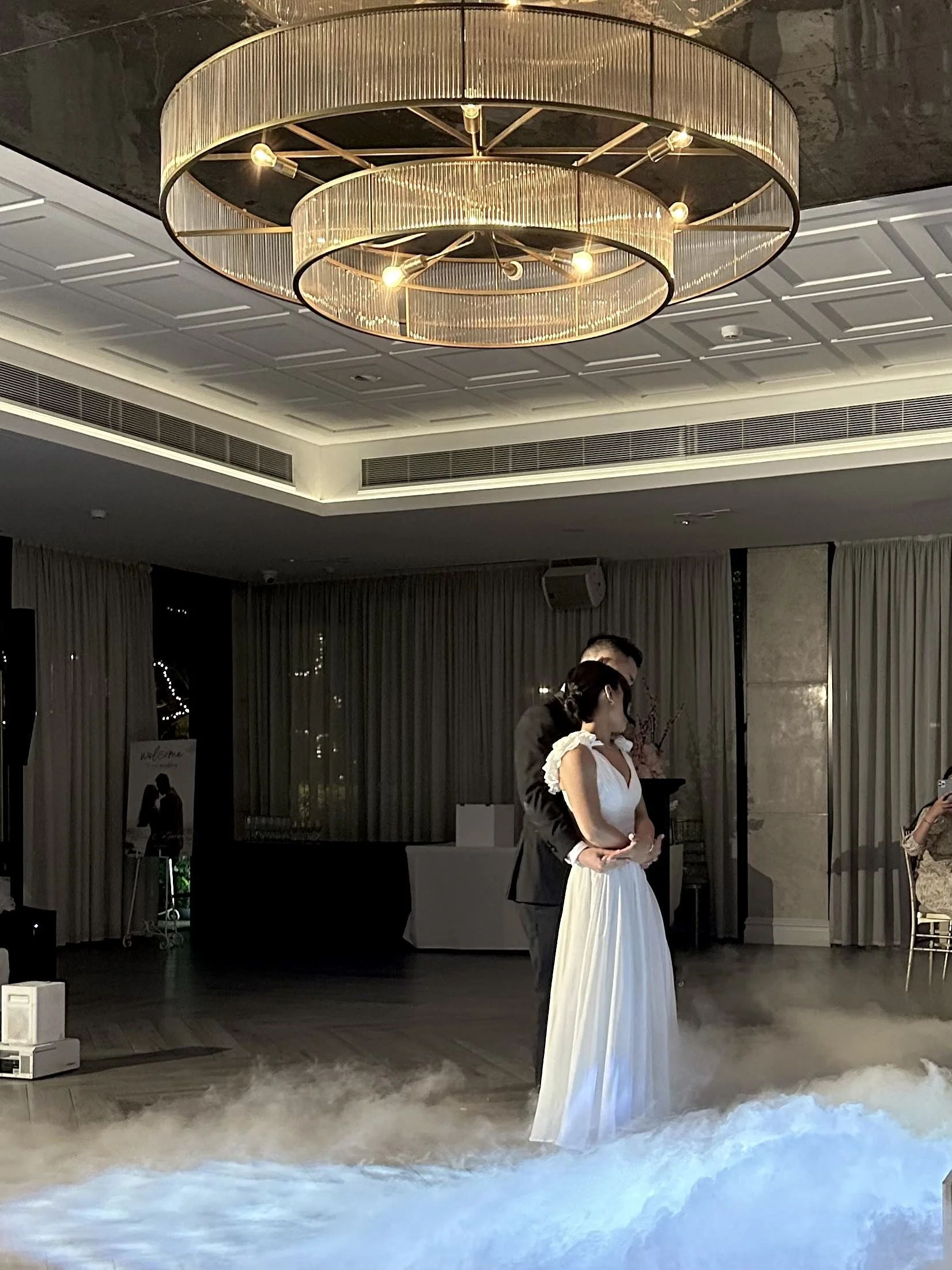 Romantic first dance moment featuring soft smoke effects beneath a glowing chandelier 