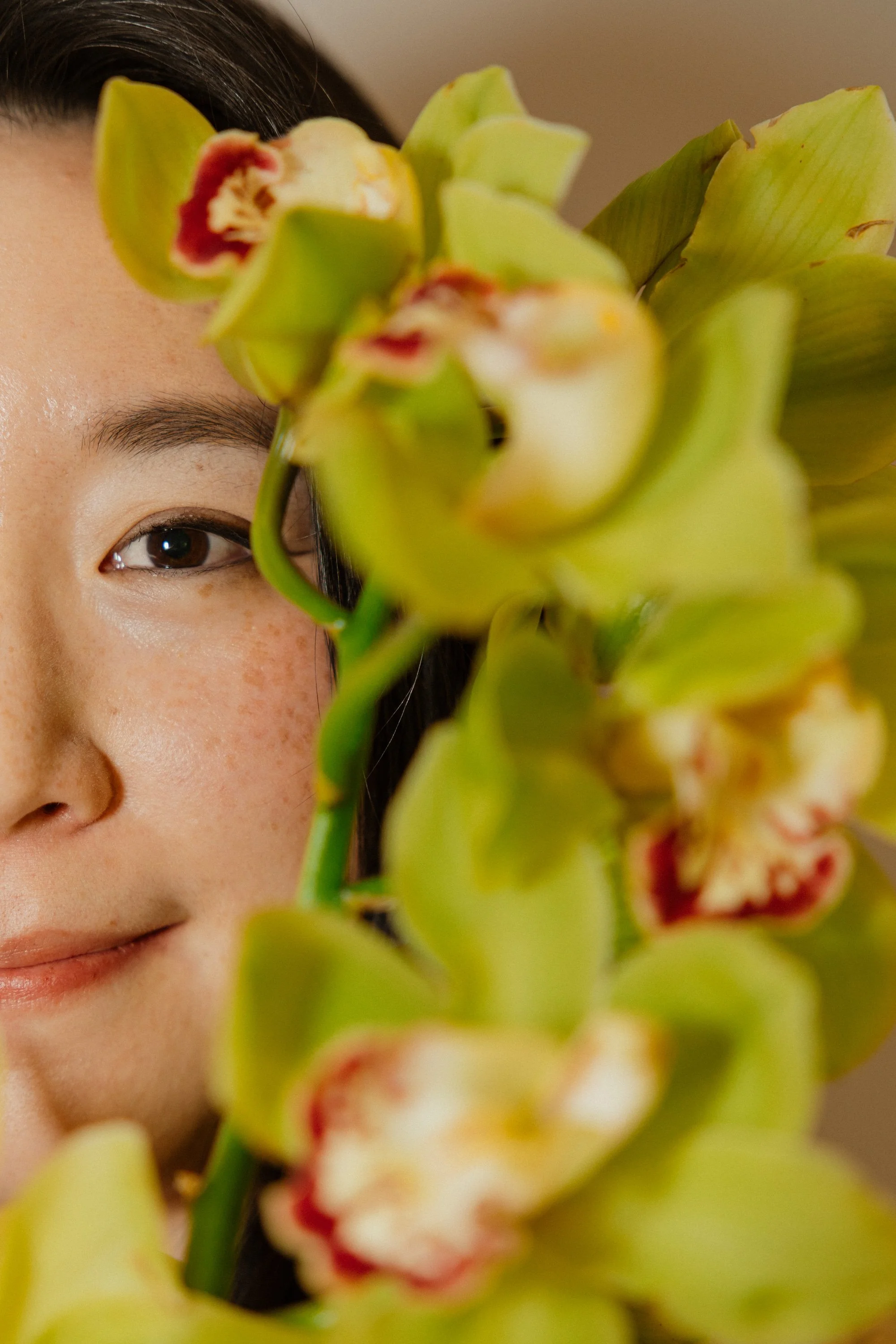 Founder of Butterfly's Rest Floral Design Studio partially framed by green orchids with red and white centers.