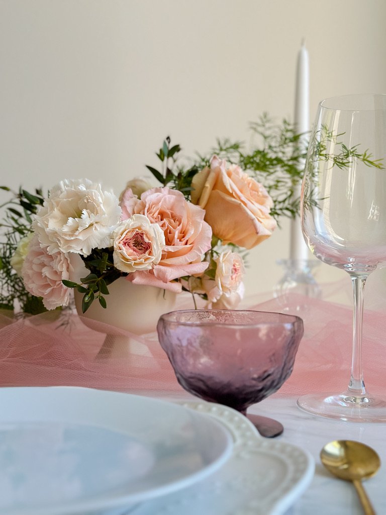 Elegant table setting with a floral centerpiece of pink and white roses, with a tall tapered candle in the background.