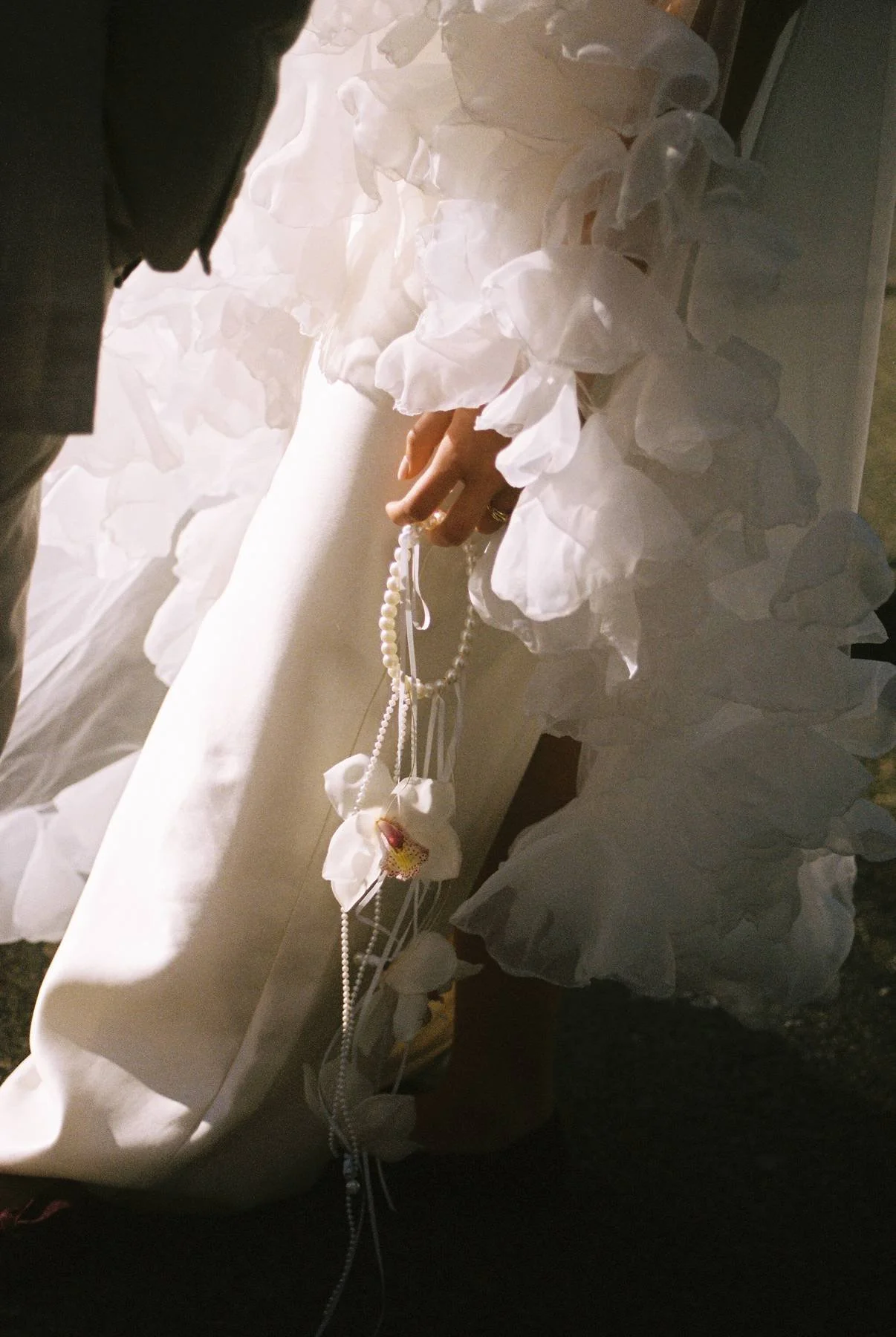 Bride holding pearl strands with a white orchid bloom against her wedding dress.