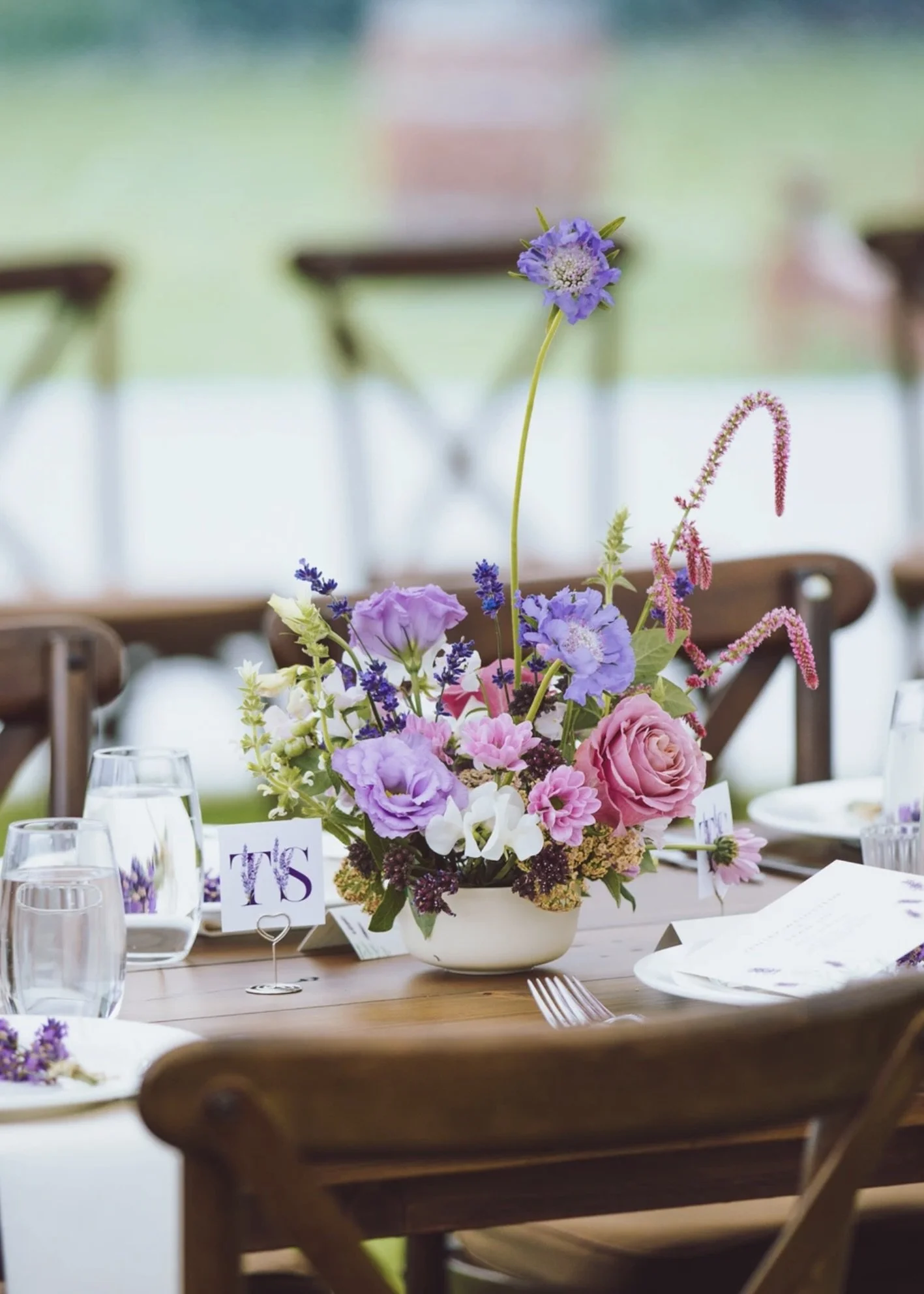 Colorful garden-inspired wedding centerpiece featuring lavender, pink, white, and burgundy seasonal blooms arranged with airy movement and sculptural detail. Floral design by Butterfly’s Rest. Photography by MXBloom Films.