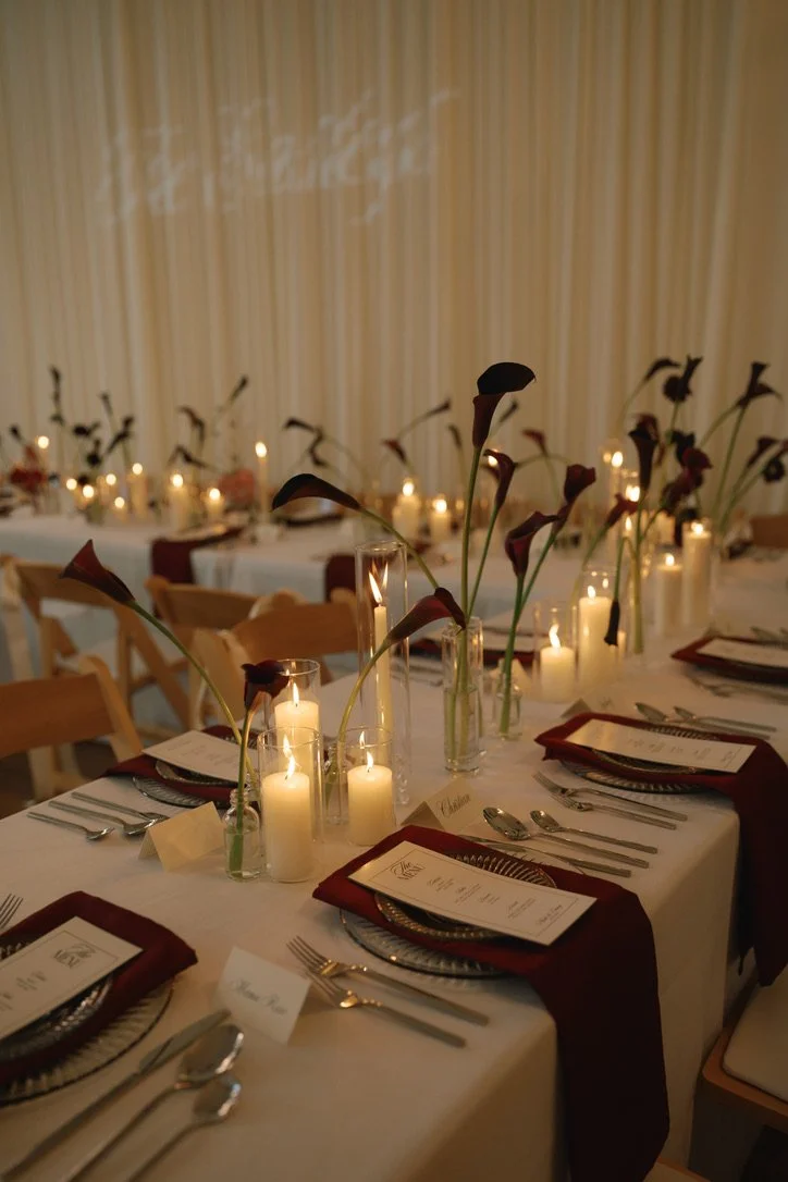 Moody, candlelit wedding reception with minimalist bud vase arrangements of deep burgundy calla lilies lining long reception tables at 210 Seattle. Floral design by Butterfly’s Rest. Photography by Elita Coralee.