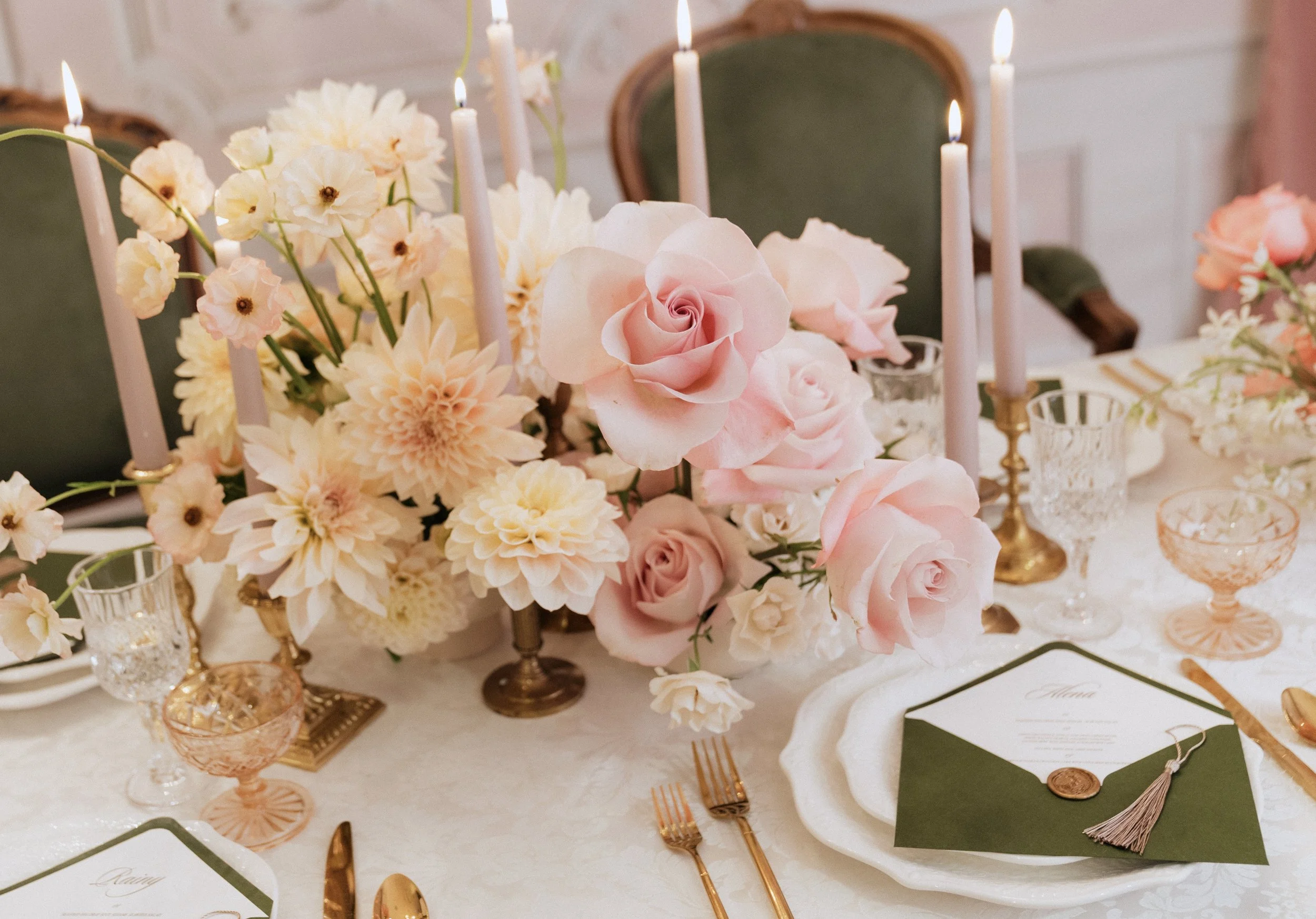 Elegant reception tablescape featuring lush pink and cream floral centerpieces, taper candles, gold flatware, and refined place settings.