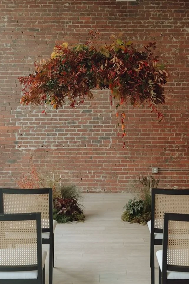 Ceremony space featuring a suspended floral installation with autumn foliage and modern event design.