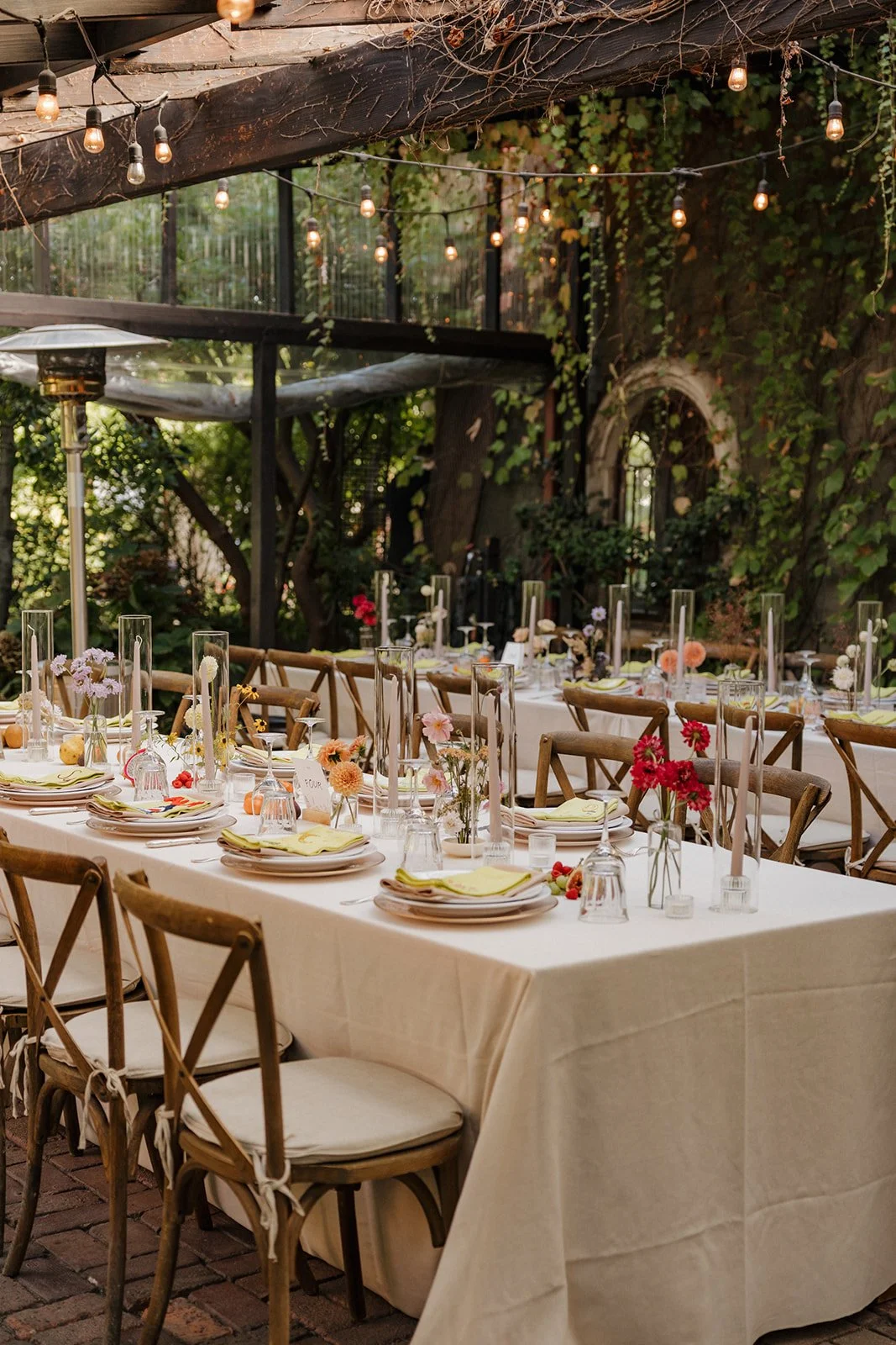 Garden dining experience featuring seasonal floral centerpieces, candlelight, and elegant place settings beneath string lights and lush greenery.