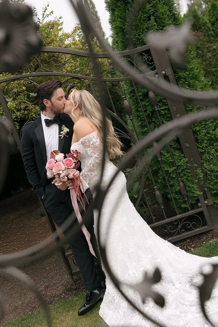 Bride and groom kissing at Columbia Collective with a romantic pink and burgundy bridal bouquet featuring garden roses, anthurium, orchids, and amaranthus. Floral design by Butterfly’s Rest. Photography by Mercedes Lou Photography.