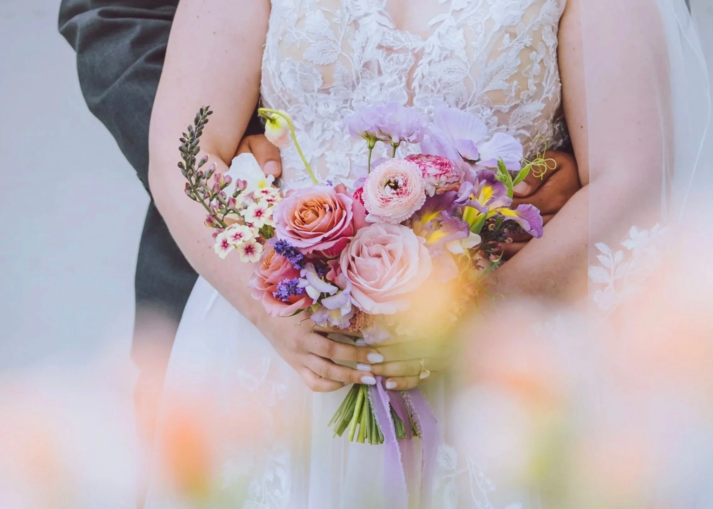 Pastel bridal bouquet featuring garden roses, ranunculus, sweet peas, and seasonal flowers tied with a lavender ribbon.