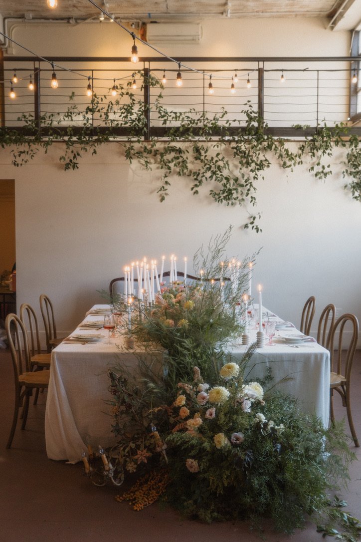 Reception tablescape featuring a meadow-inspired floral installation, candlelight, and cascading greenery in an elegant event space.