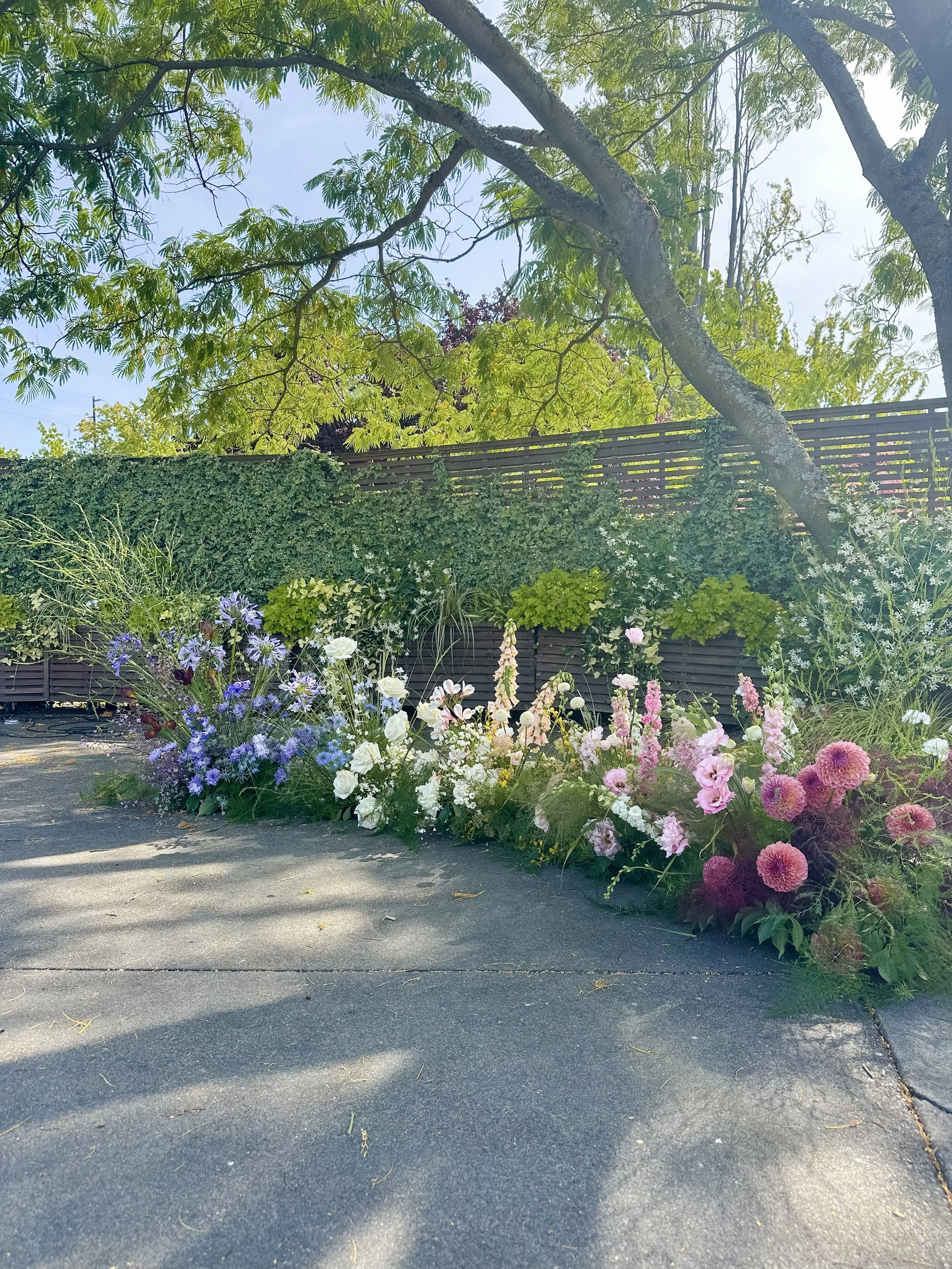 Garden-style floral installation with seasonal blooms creating an immersive meadow effect for an outdoor wedding.