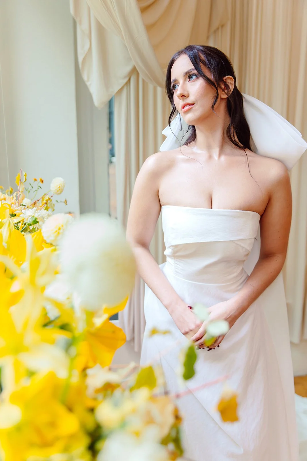 Bridal portrait featuring a modern wedding gown and abundant yellow floral installation in a light-filled event space.