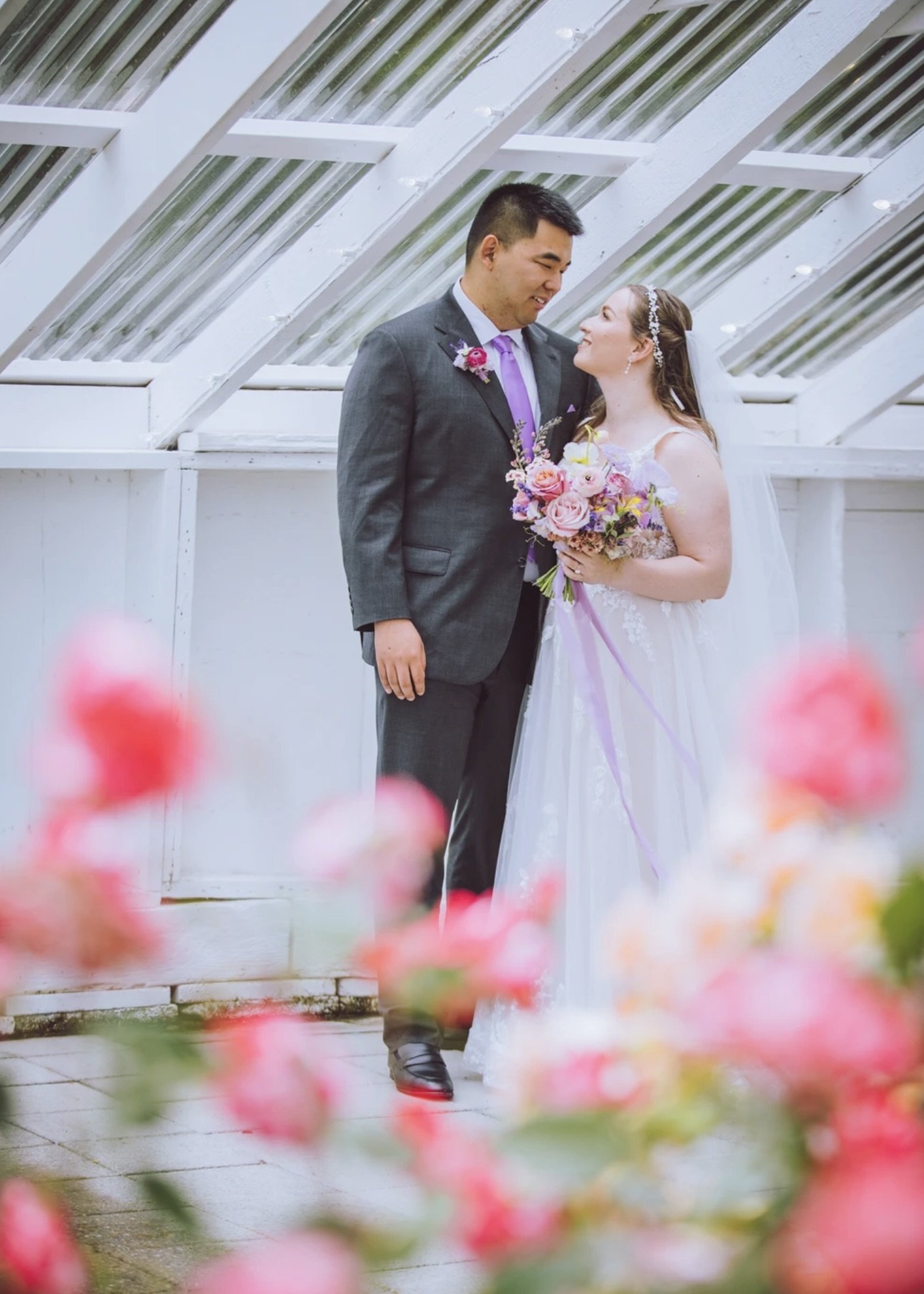 Bride and groom in a bright conservatory, featuring a colorful garden-style bridal bouquet with pastel seasonal flowers.
