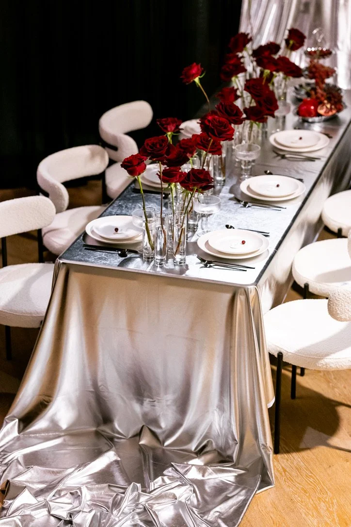 Modern wedding tablescape with sculptural red roses in glass bud vases, silver linens, white place settings, and contemporary seating. Floral design by Butterfly’s Rest. Photography by Erin Witt Photography.