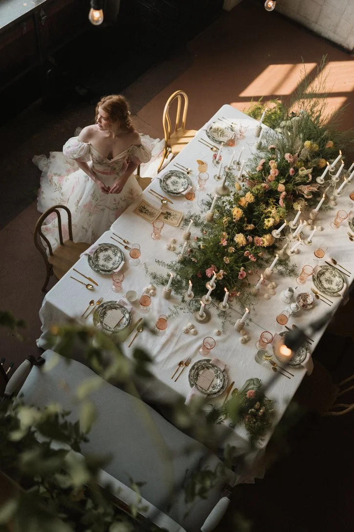 Overhead view of a romantic wedding tablescape with garden-inspired flowers, greenery, taper candles, and vintage place settings at Sole Repair Shop. Floral design by Butterfly’s Rest. Photography by Soko Photos.