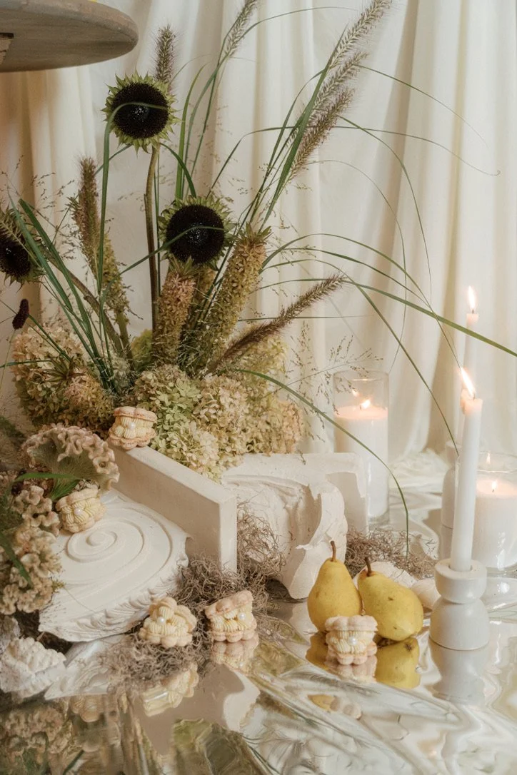 Editorial wedding tablescape with sculptural dried florals, dark sunflowers, ornamental grasses, pears, and candlelight. Floral design by Butterfly’s Rest. Photography by Amy Law Photography.