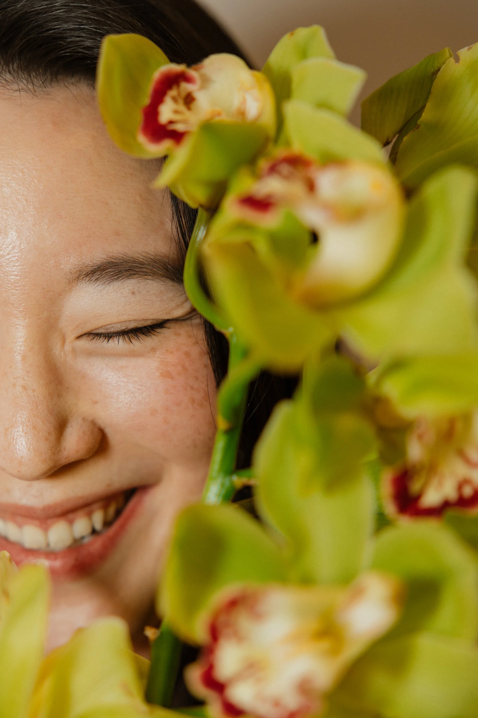 Smiling founder of Butterfly's Rest Floral Design Studio partially framed by green orchids with red and white centers.