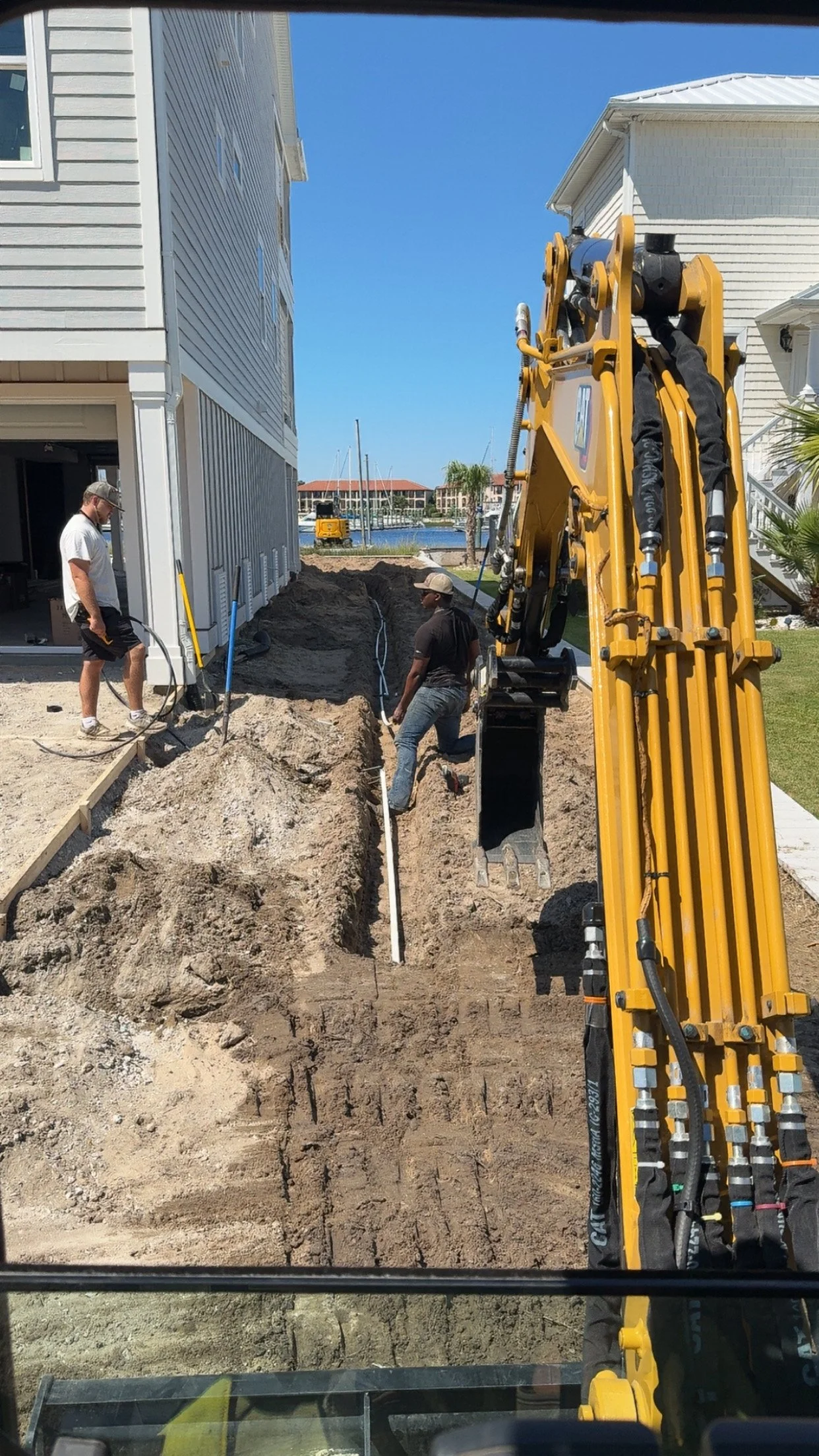 Construction workers installing underground pipes outside a house with a waterfront view.