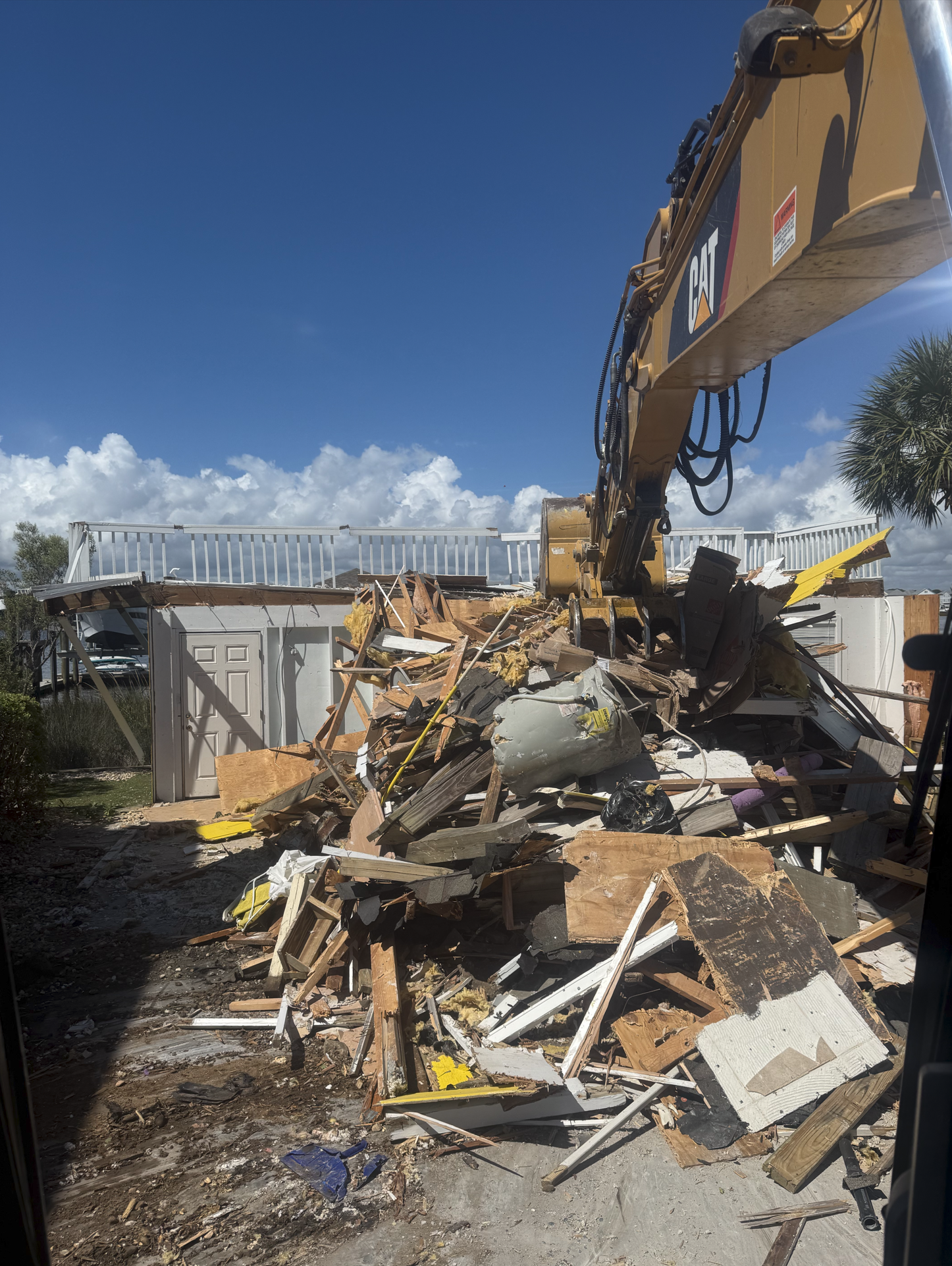 Construction equipment demolishing a building with debris and wood scattered on the ground under a blue sky.
