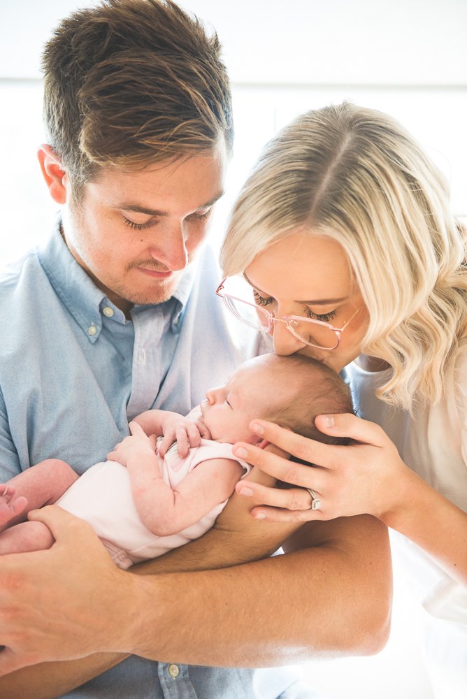 A couple holding a newborn baby, with the woman gently kissing the baby's head.