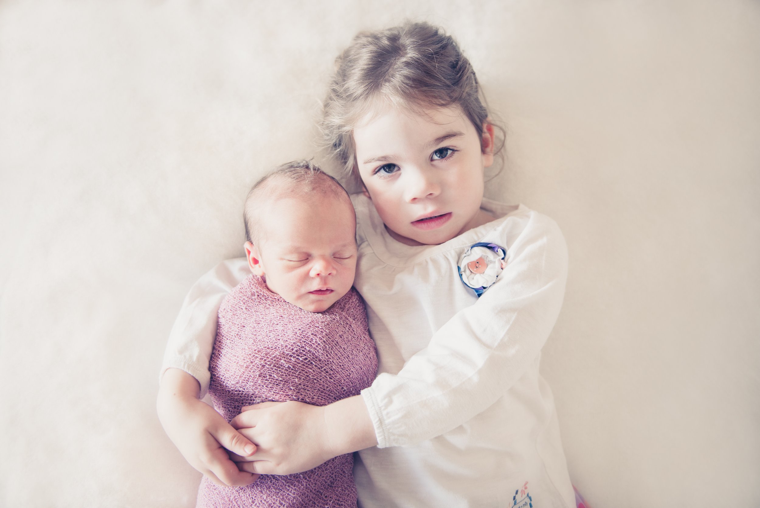 A young girl holding a sleeping newborn baby on a light-colored surface.