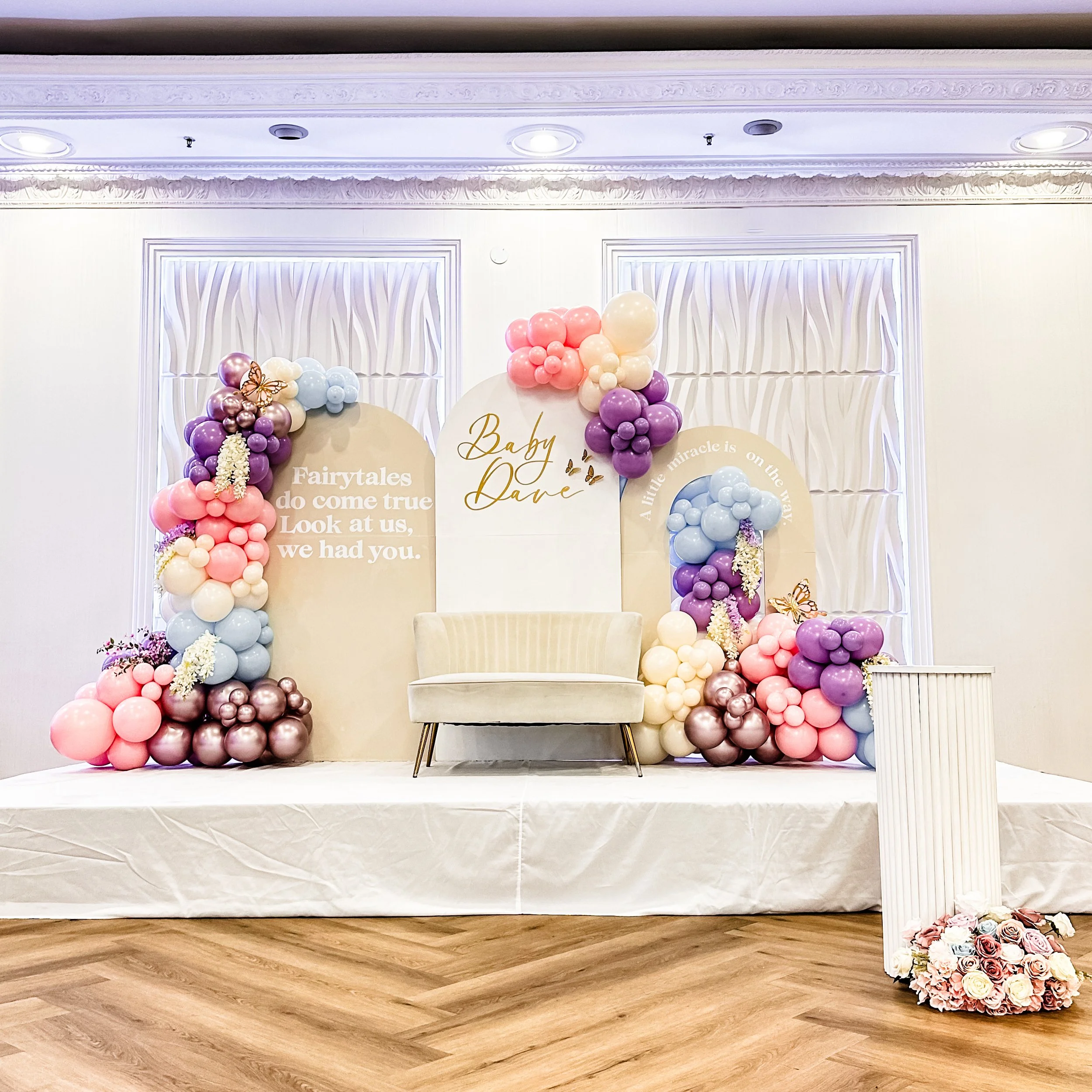Decorative stage set with pastel balloons, floral arrangements, and backdrop with quotes for a baby shower or celebration.