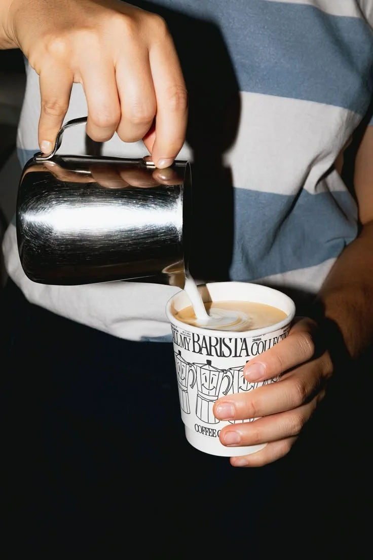 Person pouring steamed milk into a cup of coffee, creating latte art.