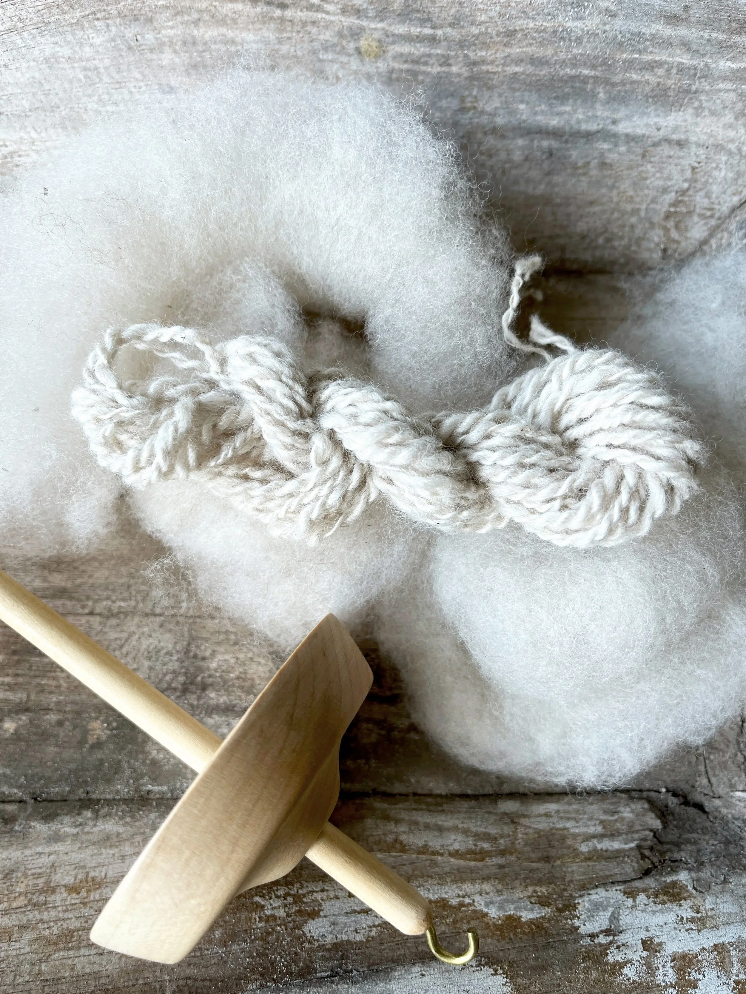 Close-up of a wooden darning mushroom and a ball of thick white yarn, surrounded by white fluffy wool fibers on a rustic wooden surface.