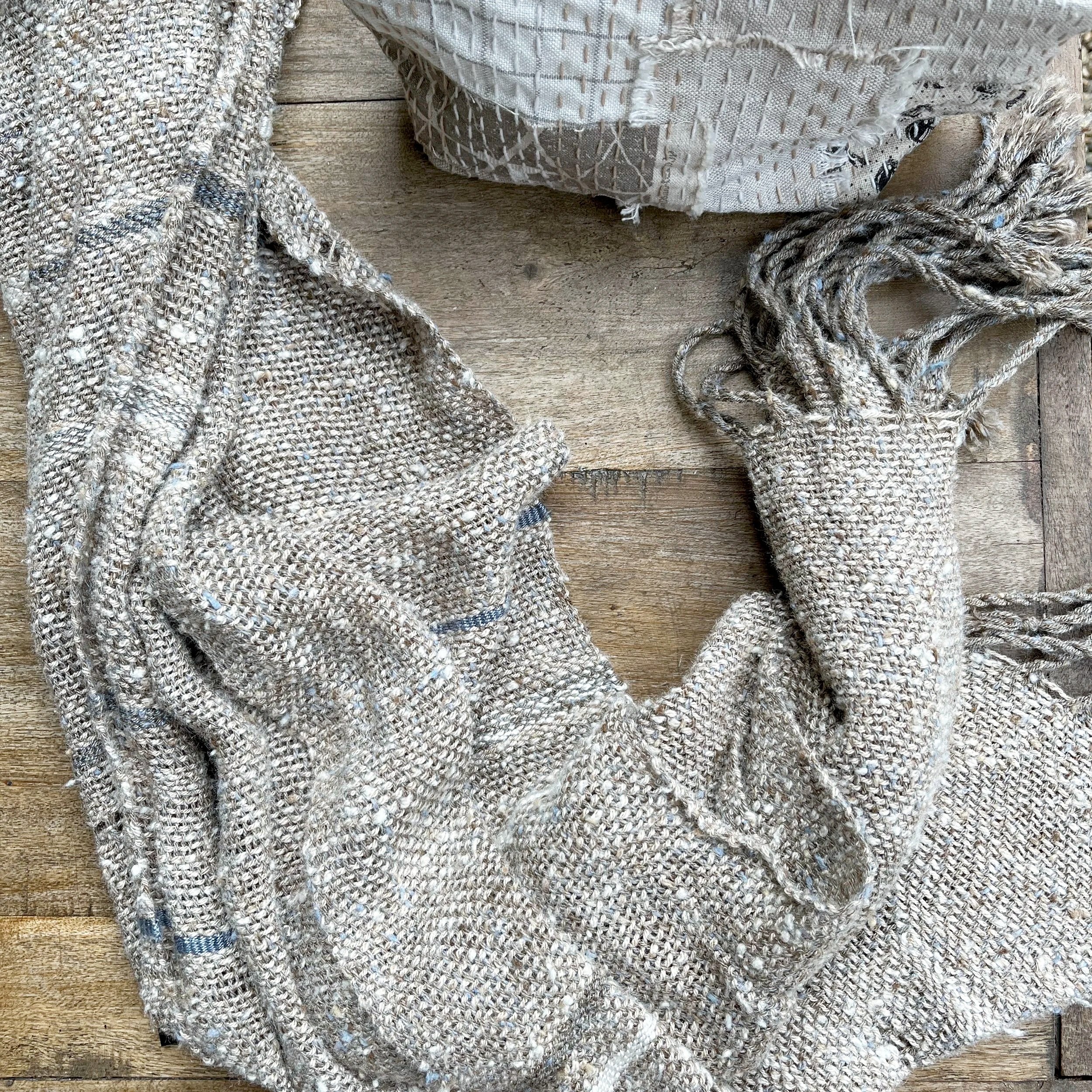 A hand woven textile made from raw silk and and patchwork cloth pouch with freehand stitching placed on a wooden surface.