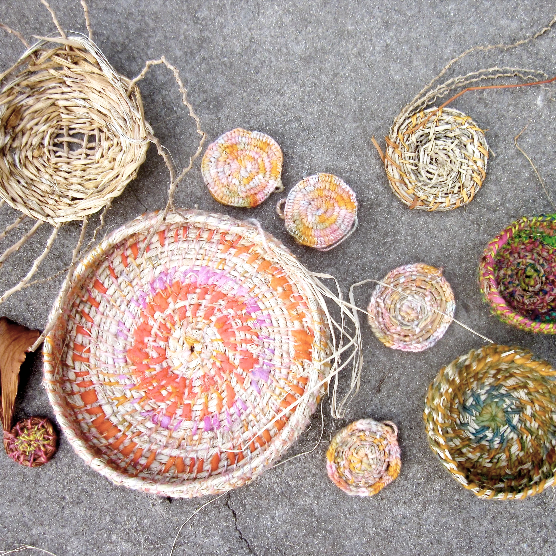 Colorful woven baskets and small woven cups arranged on a concrete surface.