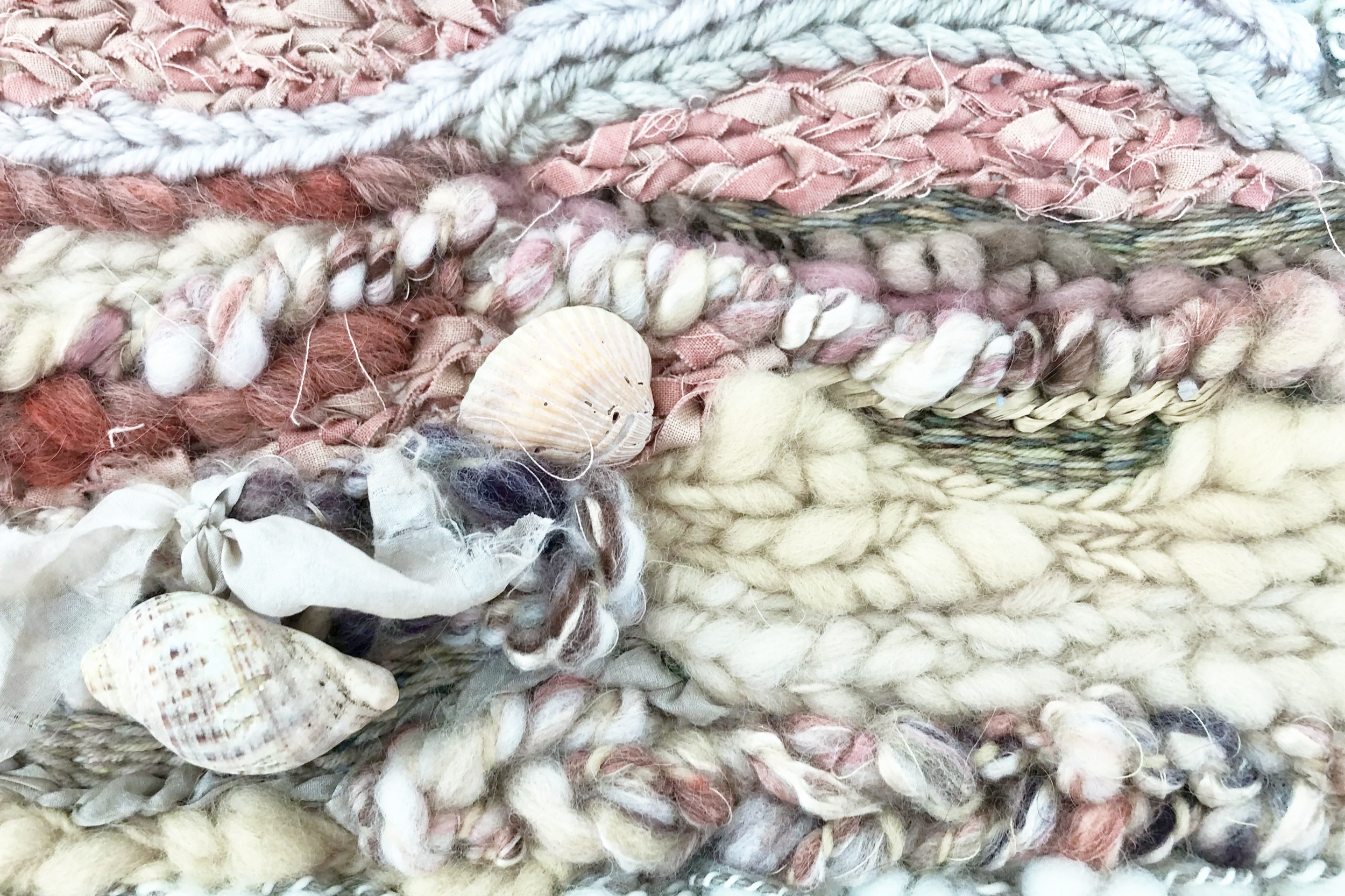Close-up of various handmade textile fibers, yarns, and shells in soft pastel colors.