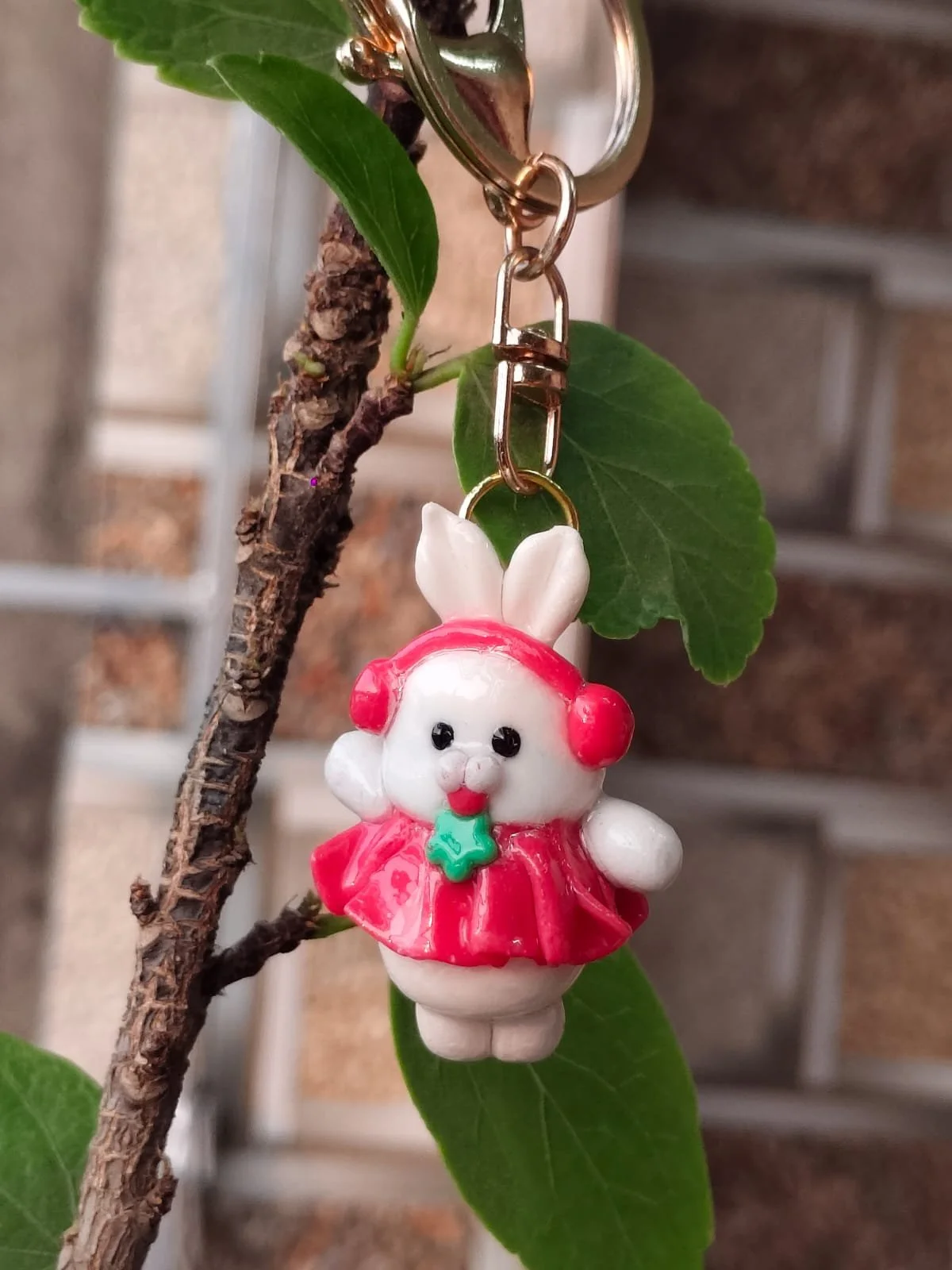A small toy figure of a bunny wearing a red dress, red earmuffs, and a red hat, hanging from a plant branch.