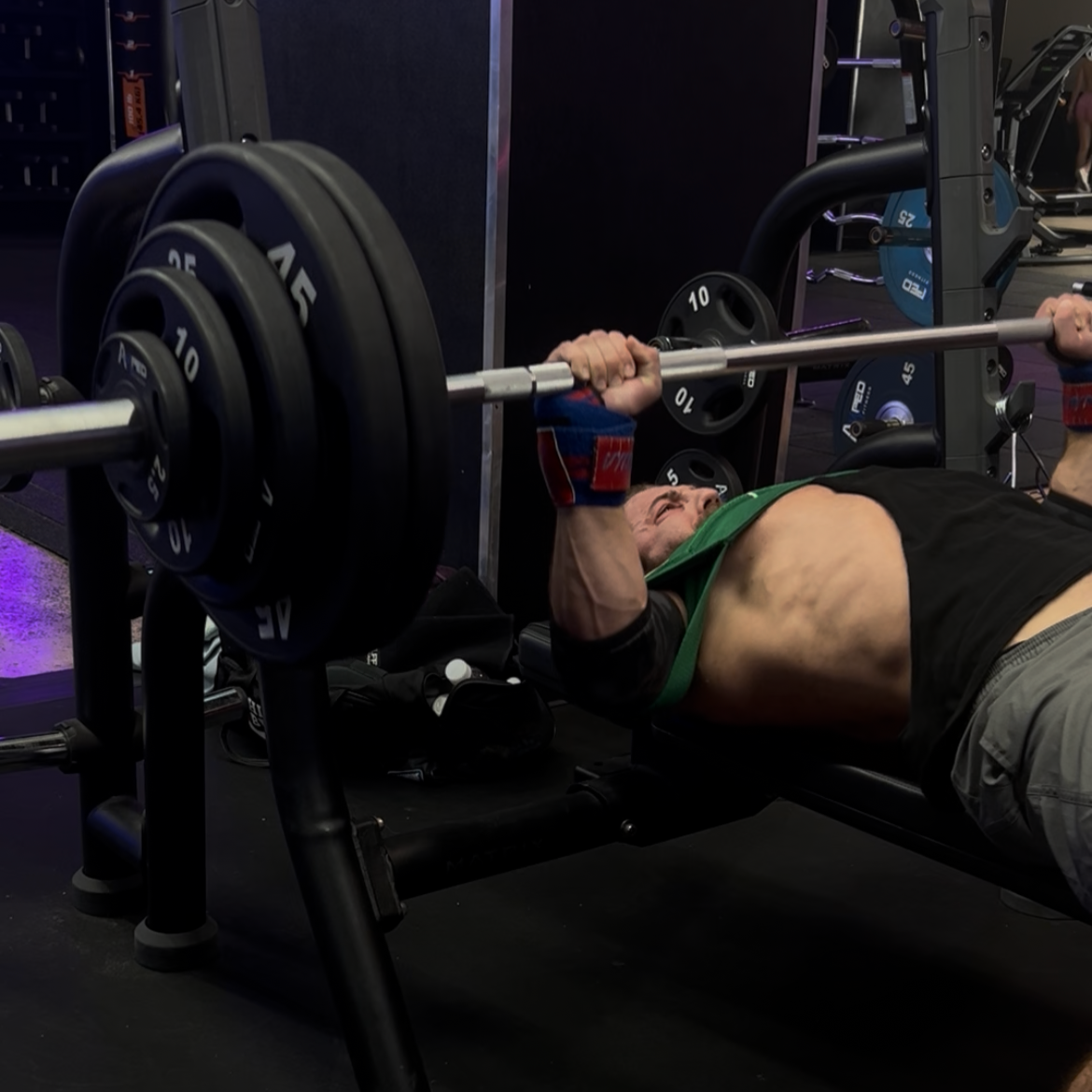 A man lying on a bench press in a gym, lifting a barbell with weights.